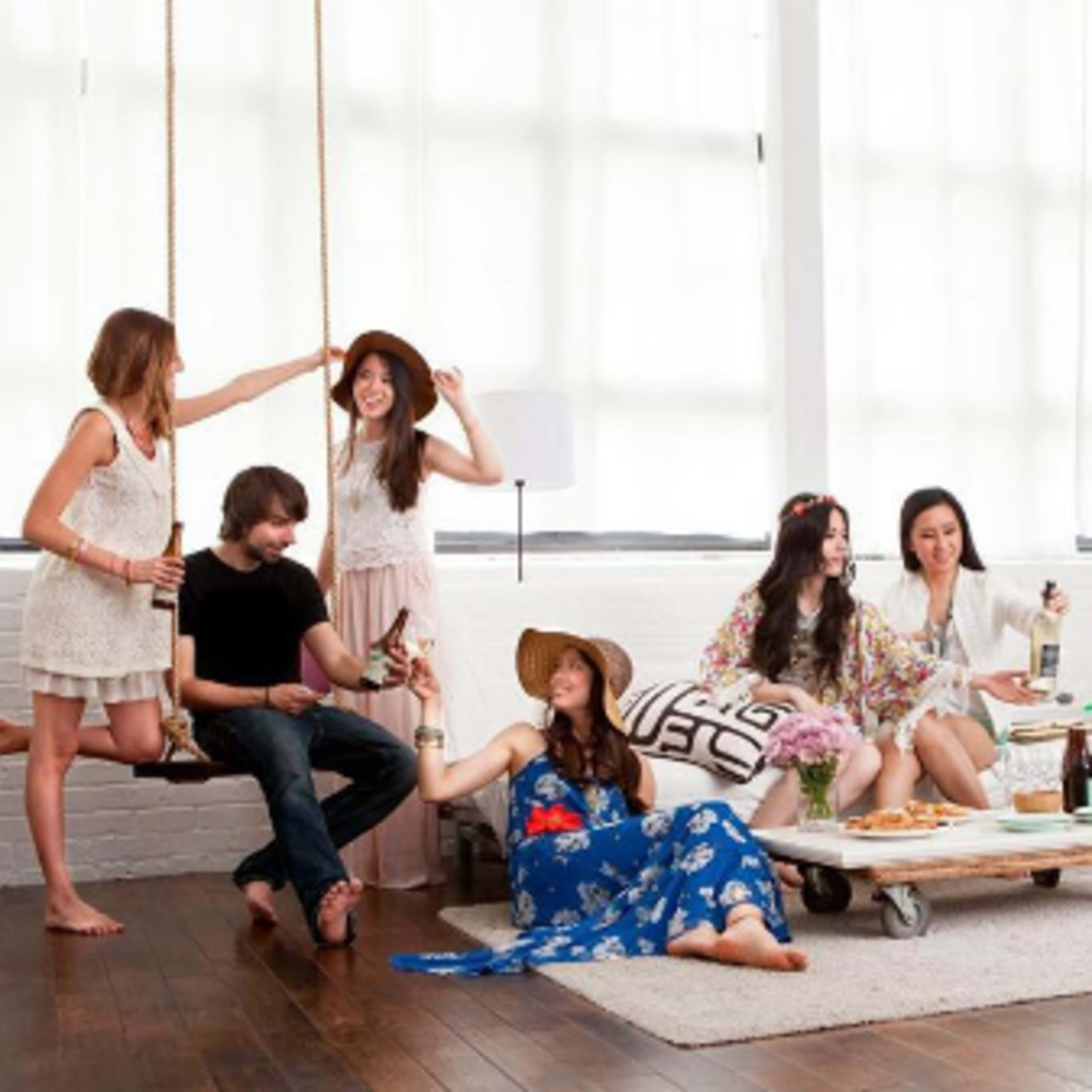 A group of eight people socializes in a bright, open space with swings, drinks, and snacks on a coffee table.