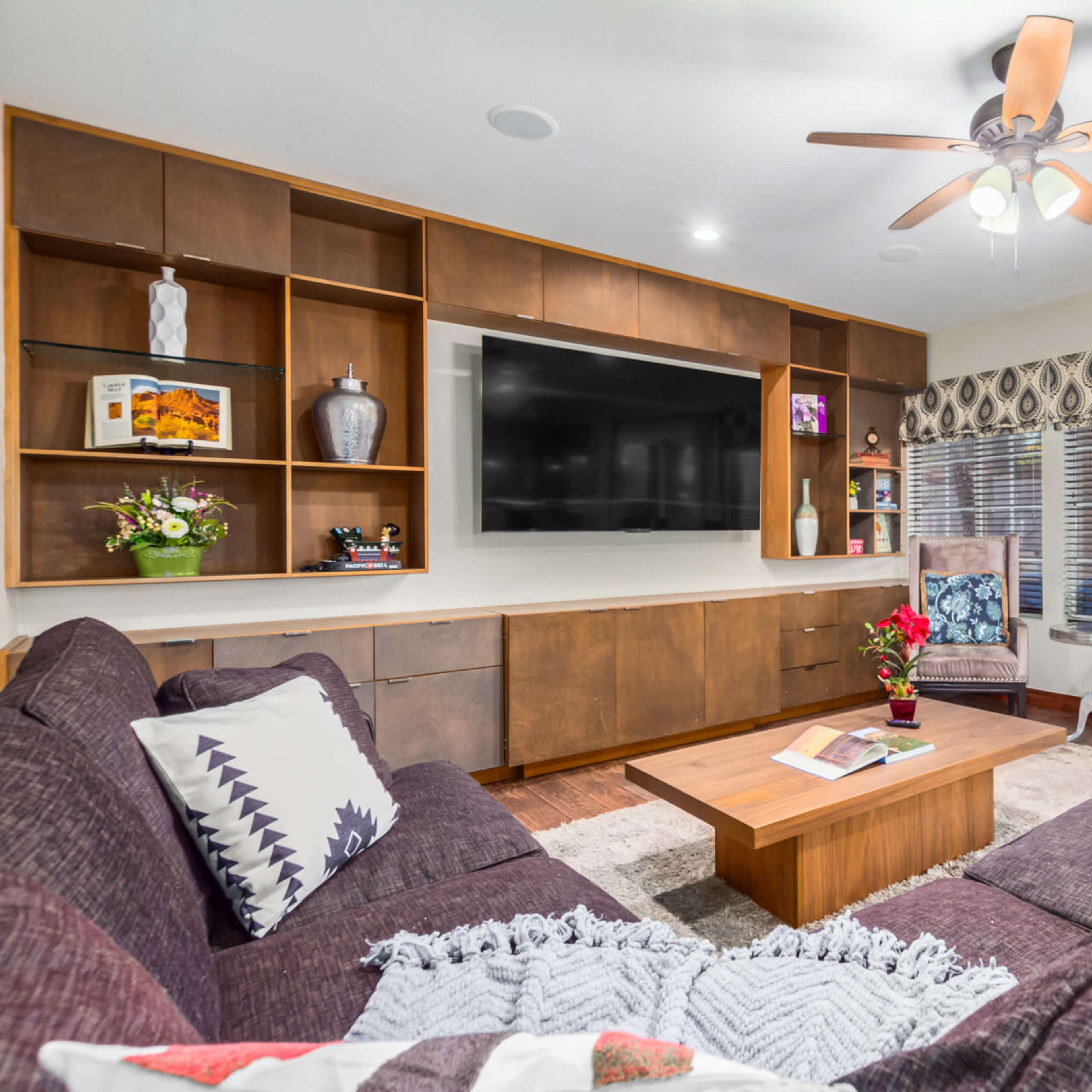 The living room features a large sectional sofa, a wooden entertainment unit with a flat-screen TV, and two armchairs, all arranged around a coffee table.