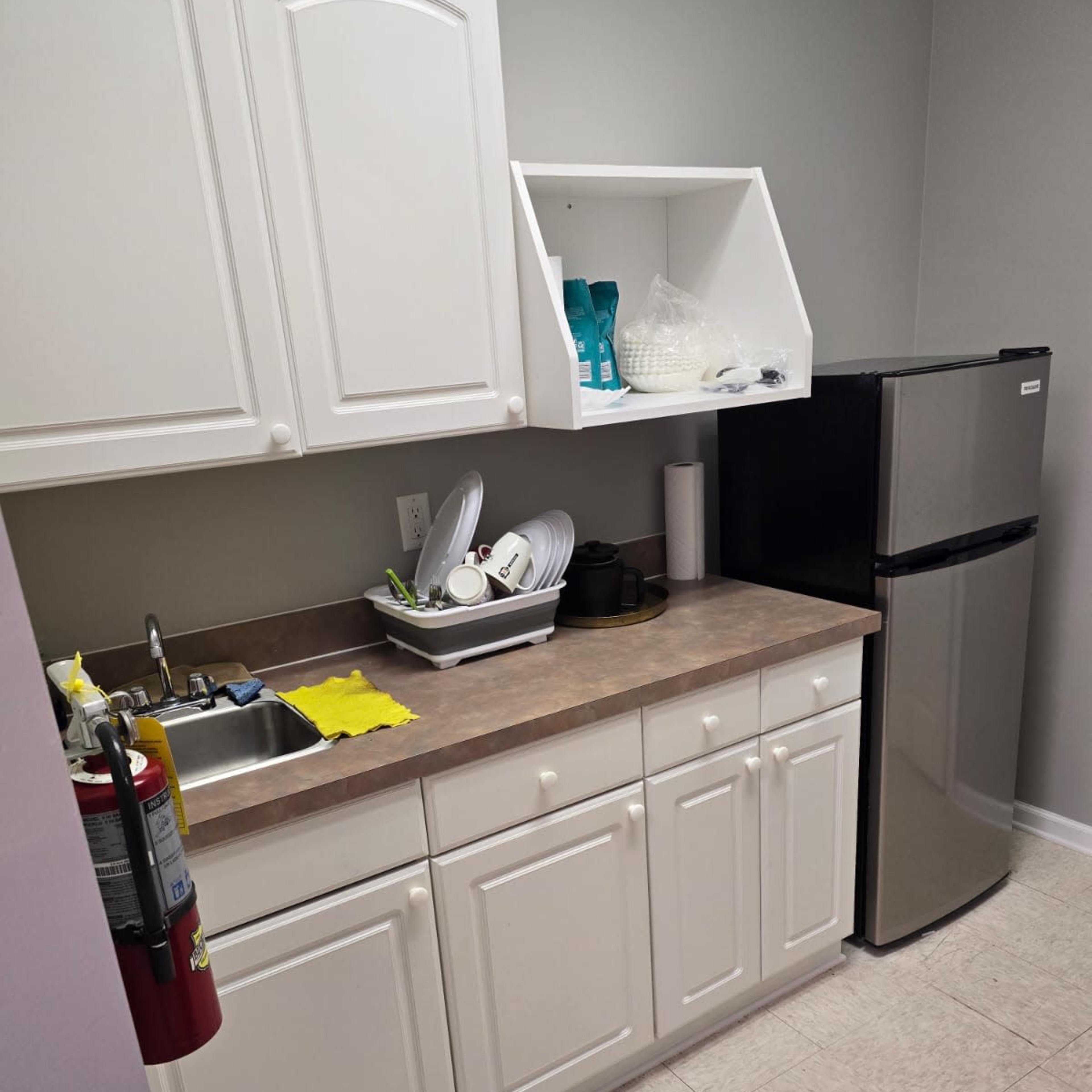 A small kitchen area with white cabinets, a stainless steel refrigerator, and a sink with dirty dishes in a bowl.