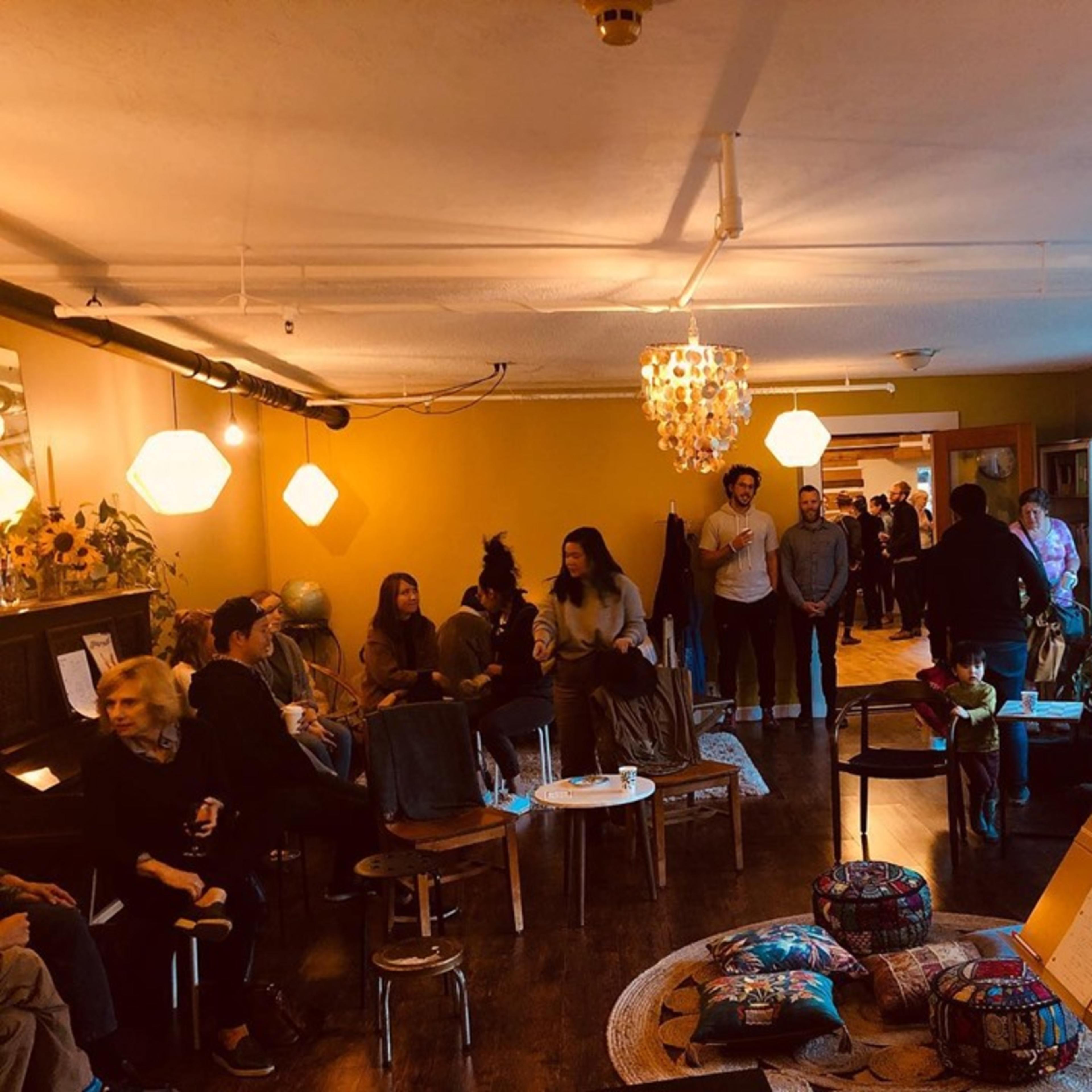 A group of people socializes in a cozy, dimly lit room adorned with plants and decorative lighting.