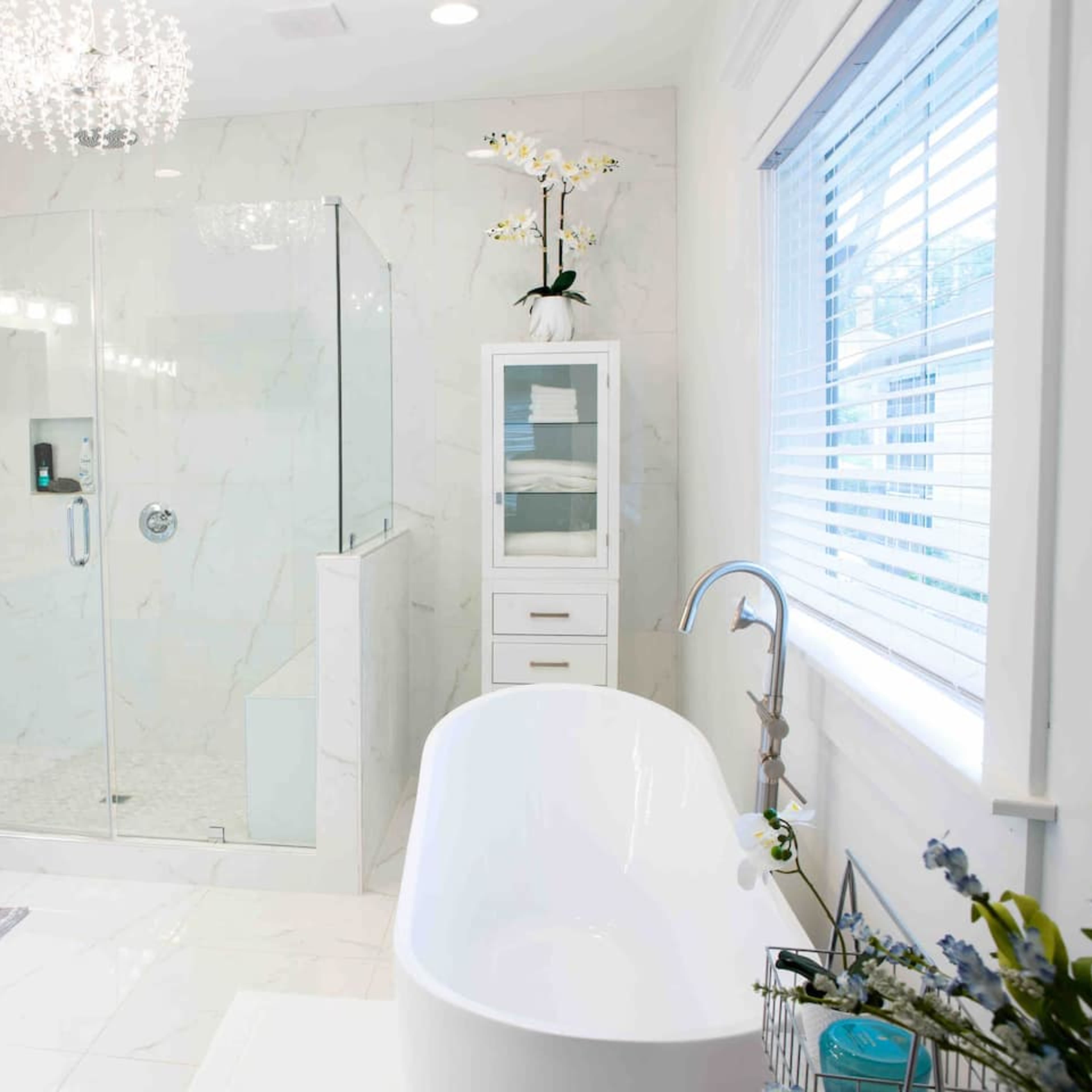 A modern bathroom featuring a glass shower, a freestanding bathtub, and white cabinetry with a marble finish.