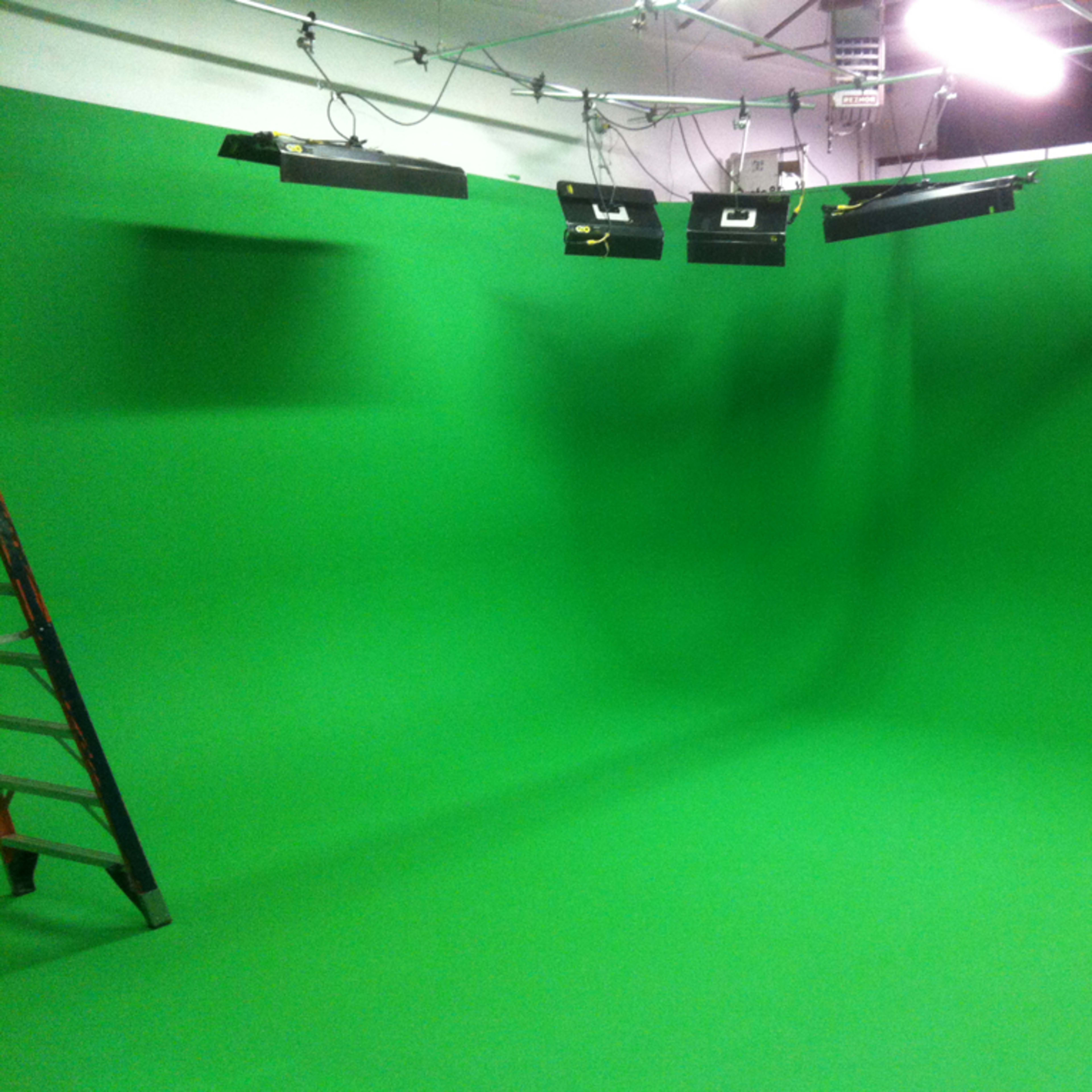 A green screen studio with a large green backdrop and lighting fixtures overhead.