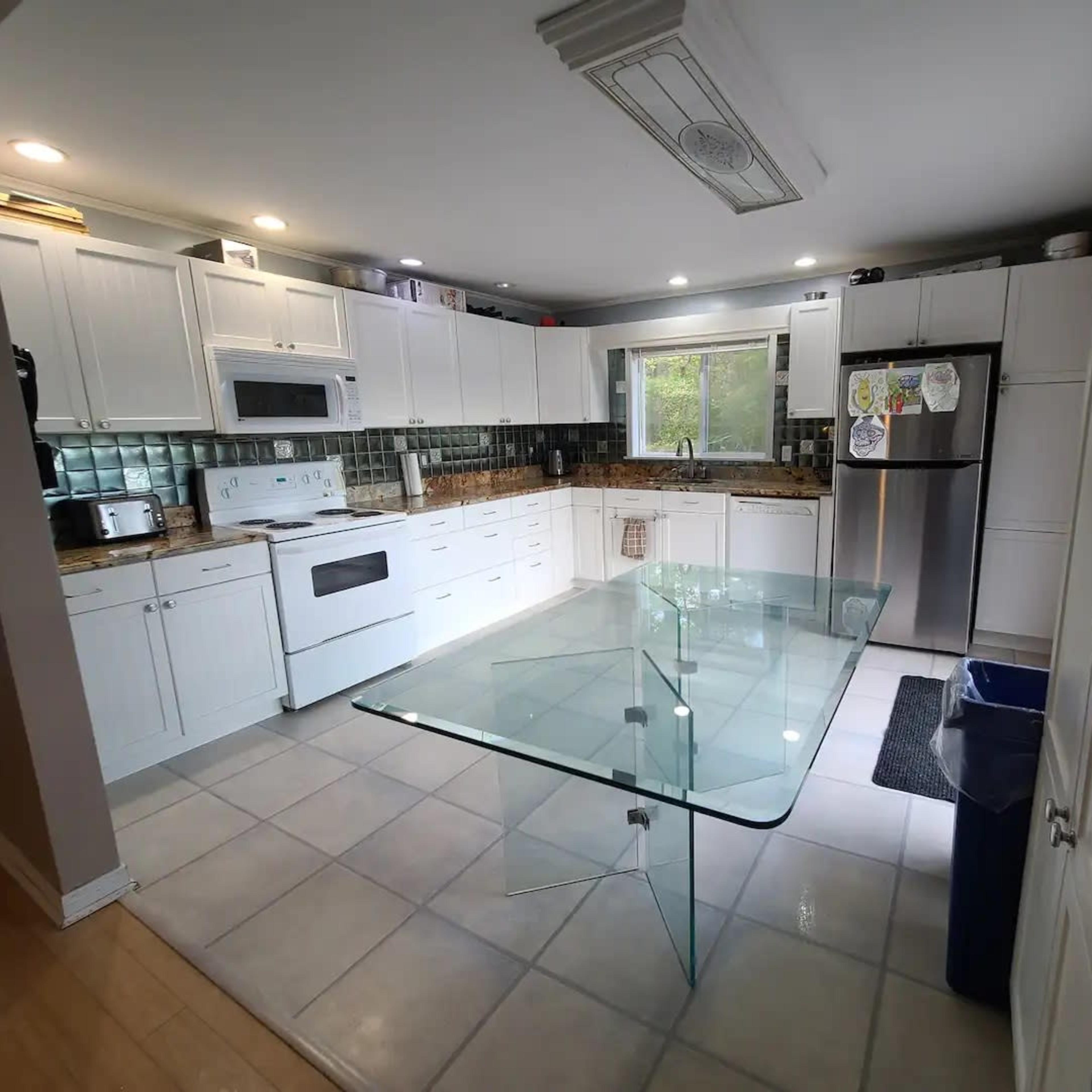 A modern kitchen features white cabinetry, stainless steel appliances, and a glass-topped table in the center.