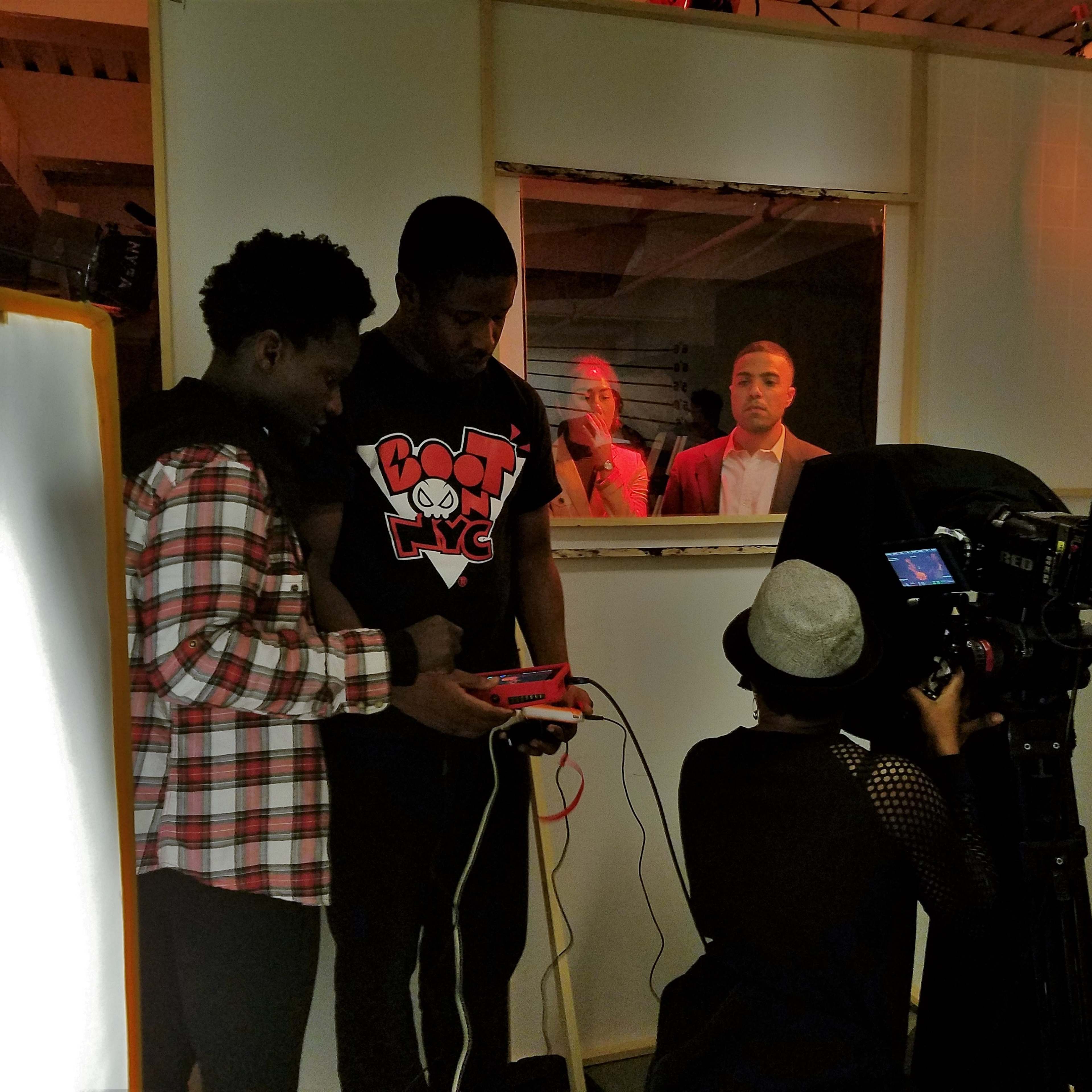 A group of people is engaged in filming behind a partition, with two individuals using a video game console while another stands in front of a camera.