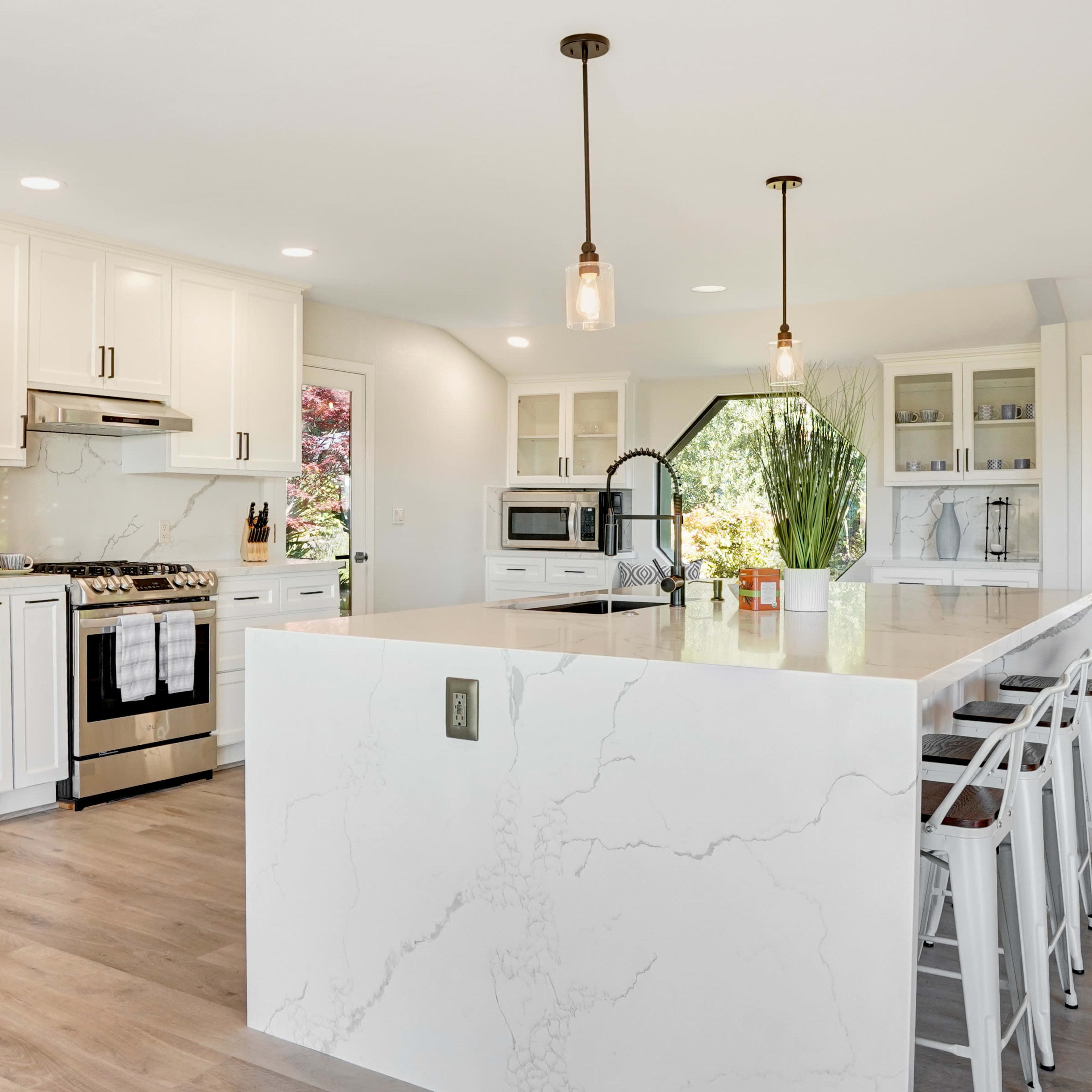 A modern kitchen features white cabinetry, stainless steel appliances, and a large island with marble-like countertops.