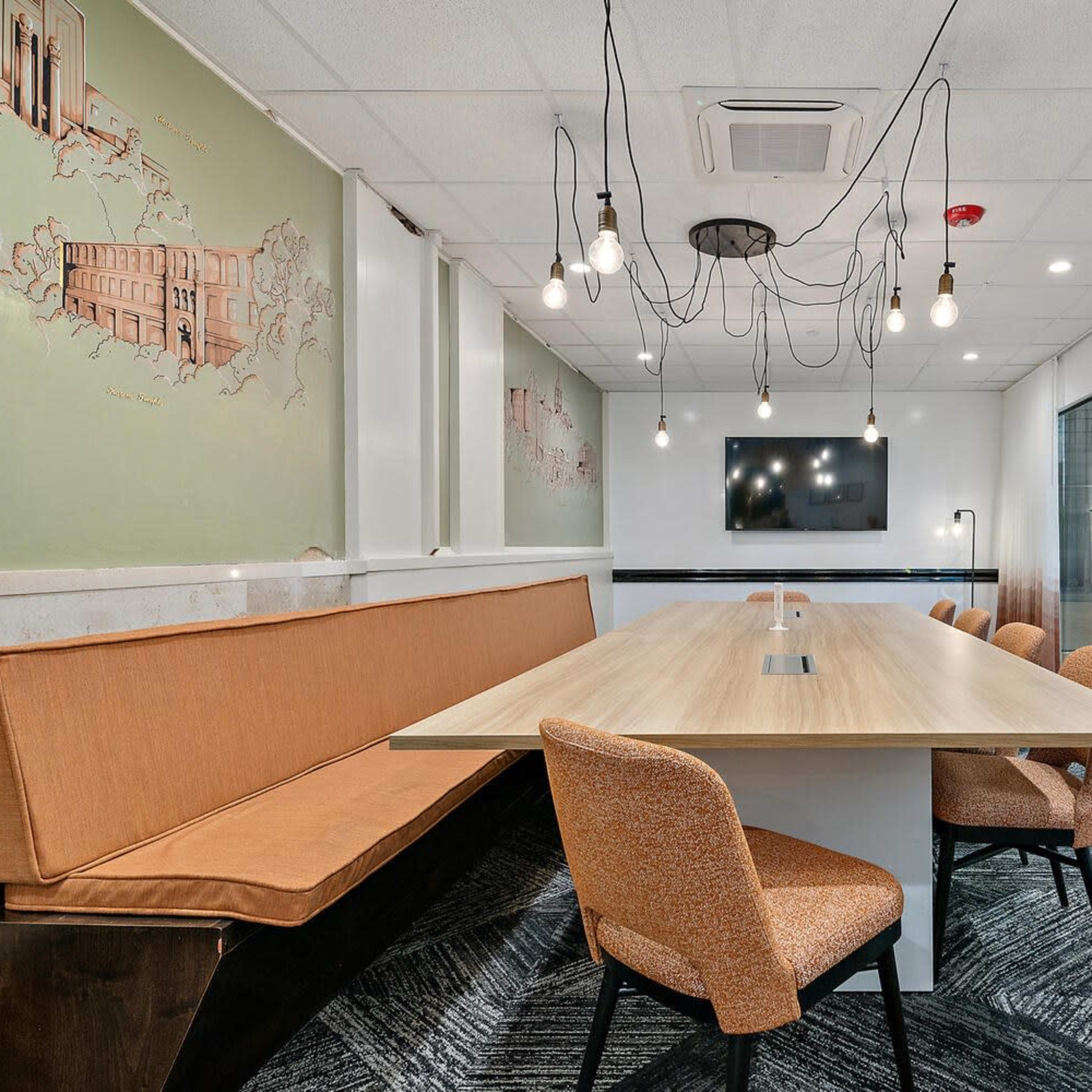 A modern conference room featuring a long wooden table surrounded by orange chairs, and decorative wall murals in a well-lit space.
