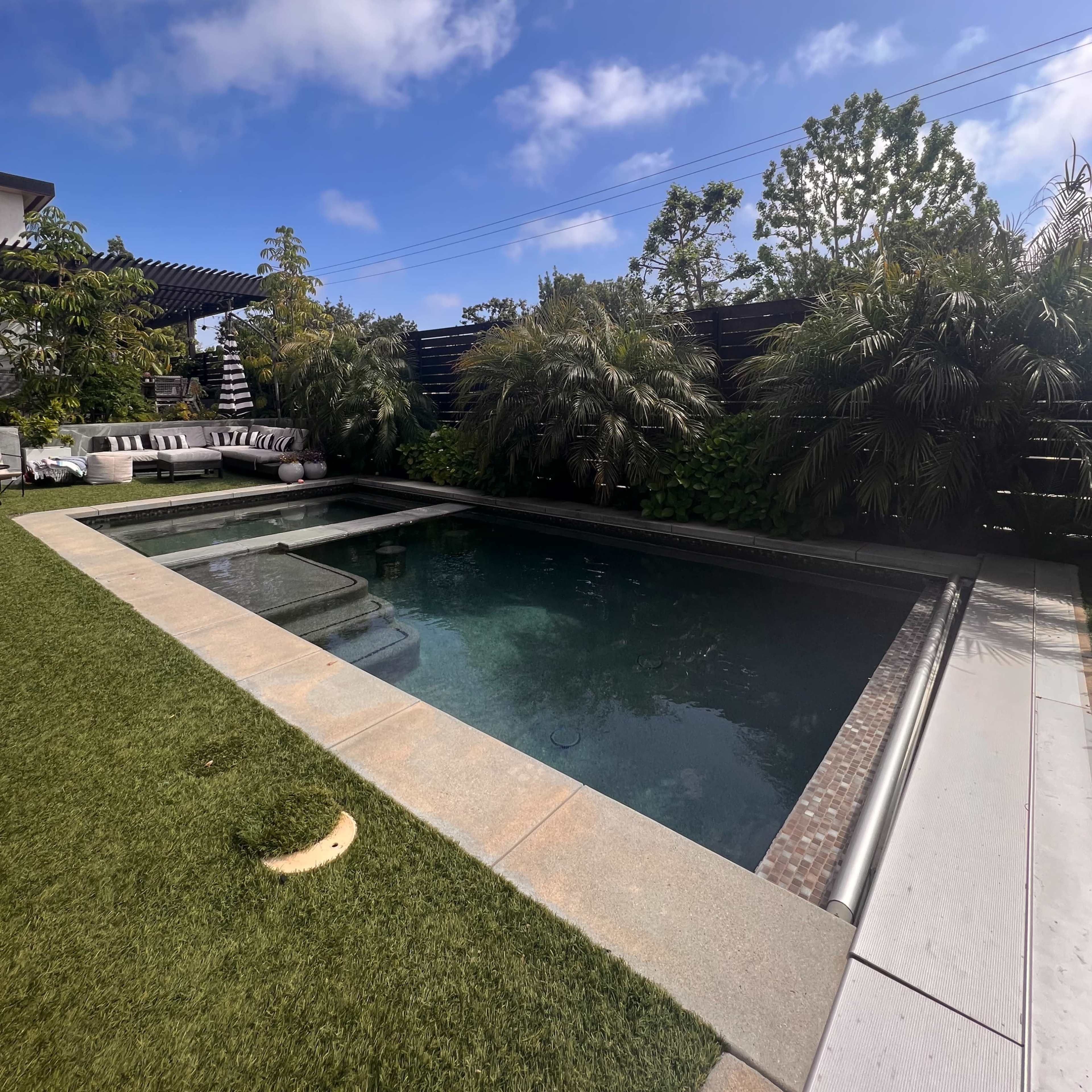A modern backyard with a swimming pool surrounded by greenery and a neatly trimmed lawn.