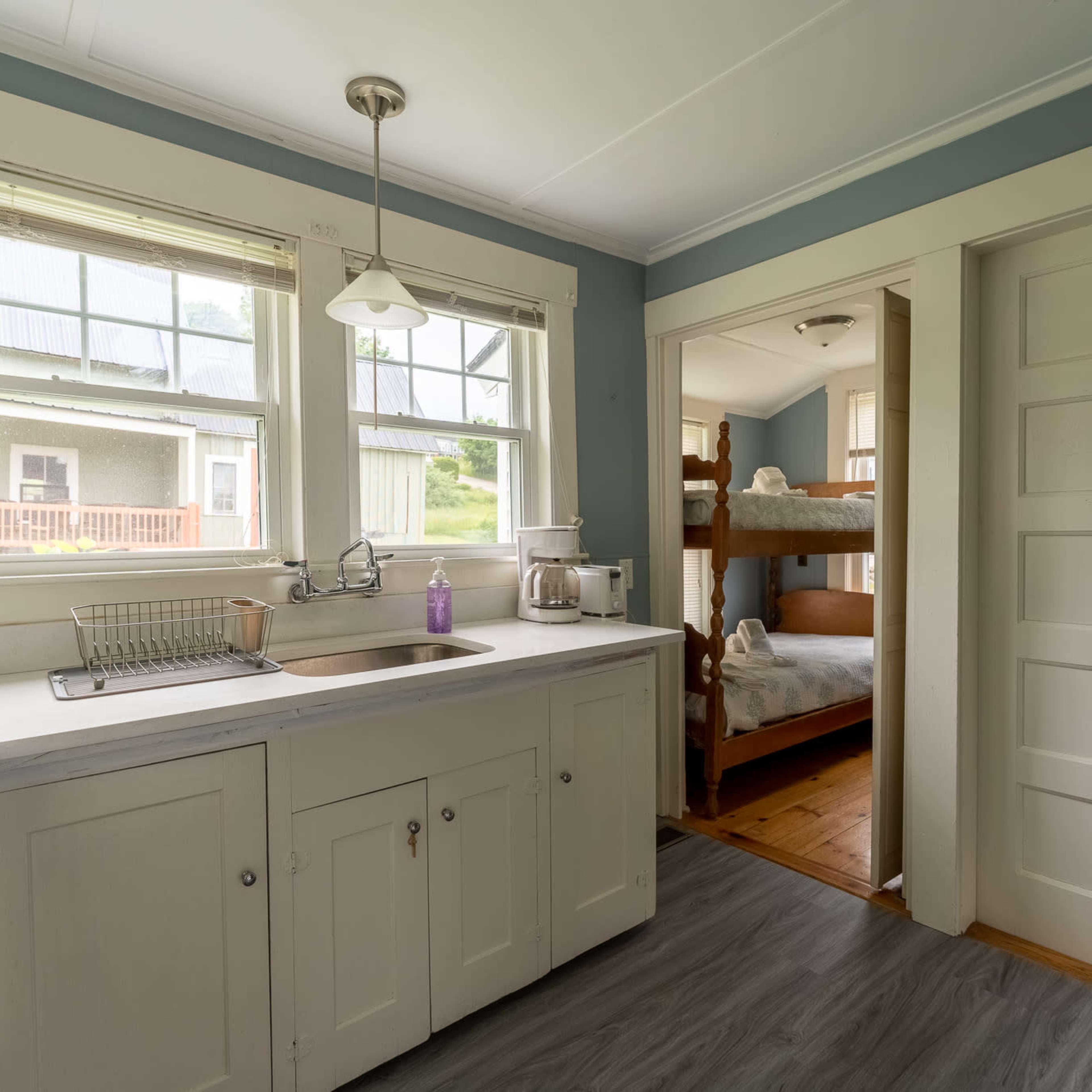 A kitchen with white cabinets, a sink, and a doorway leading to a room with bunk beds.