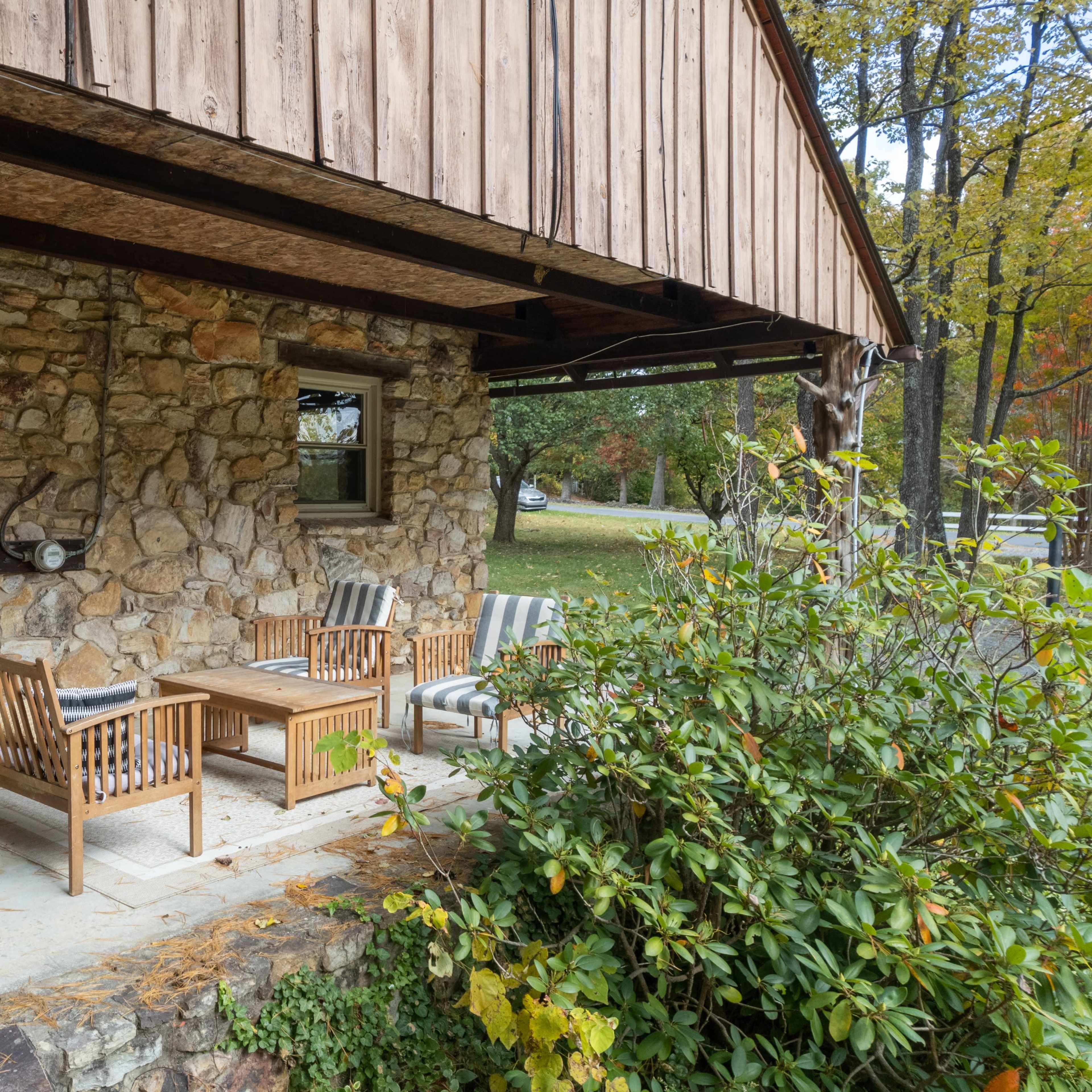 A rustic stone patio features wooden seating and a coffee table beneath an overhanging roof.