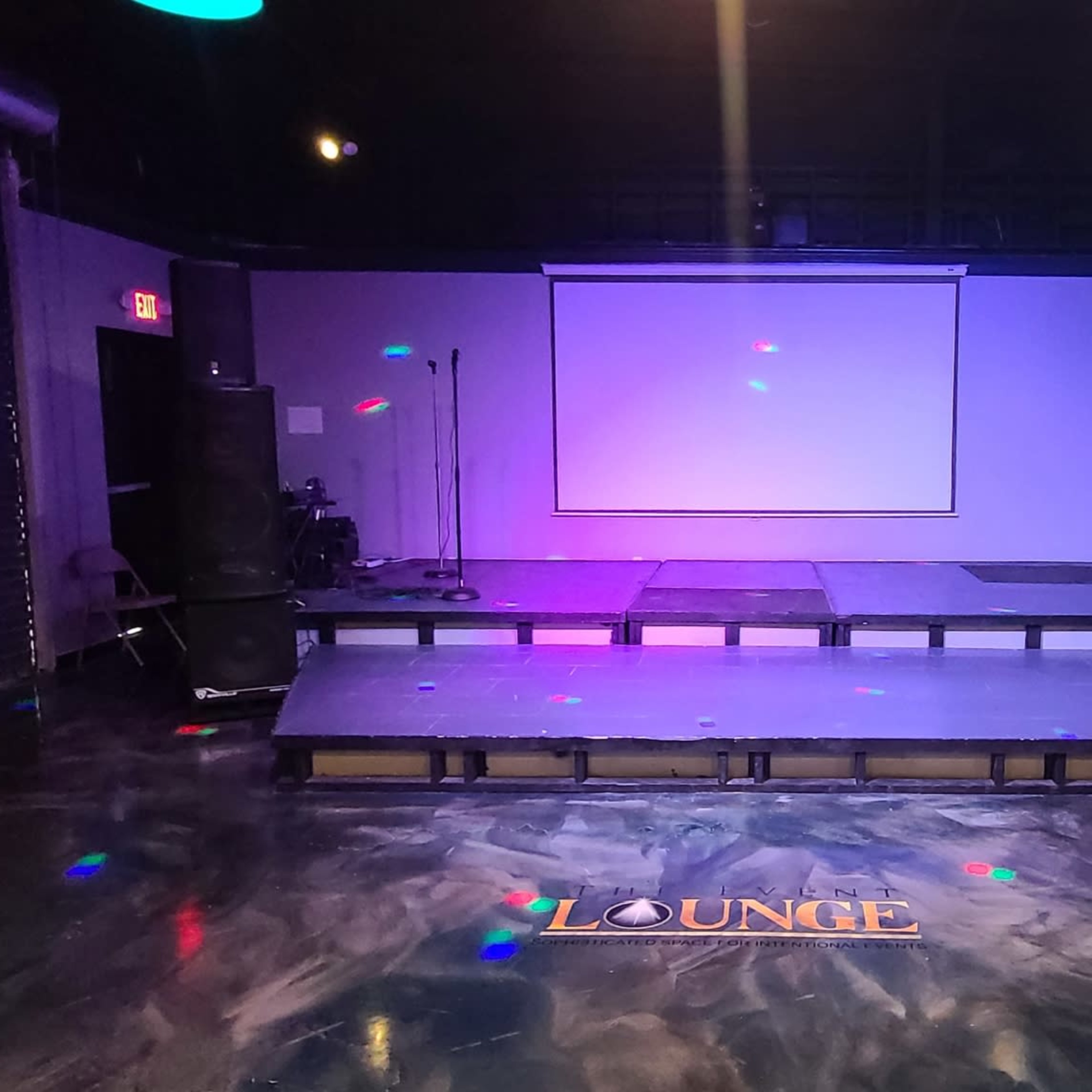 A lounge area with a raised stage, sound equipment, a large screen, and a decorative hookah setup.