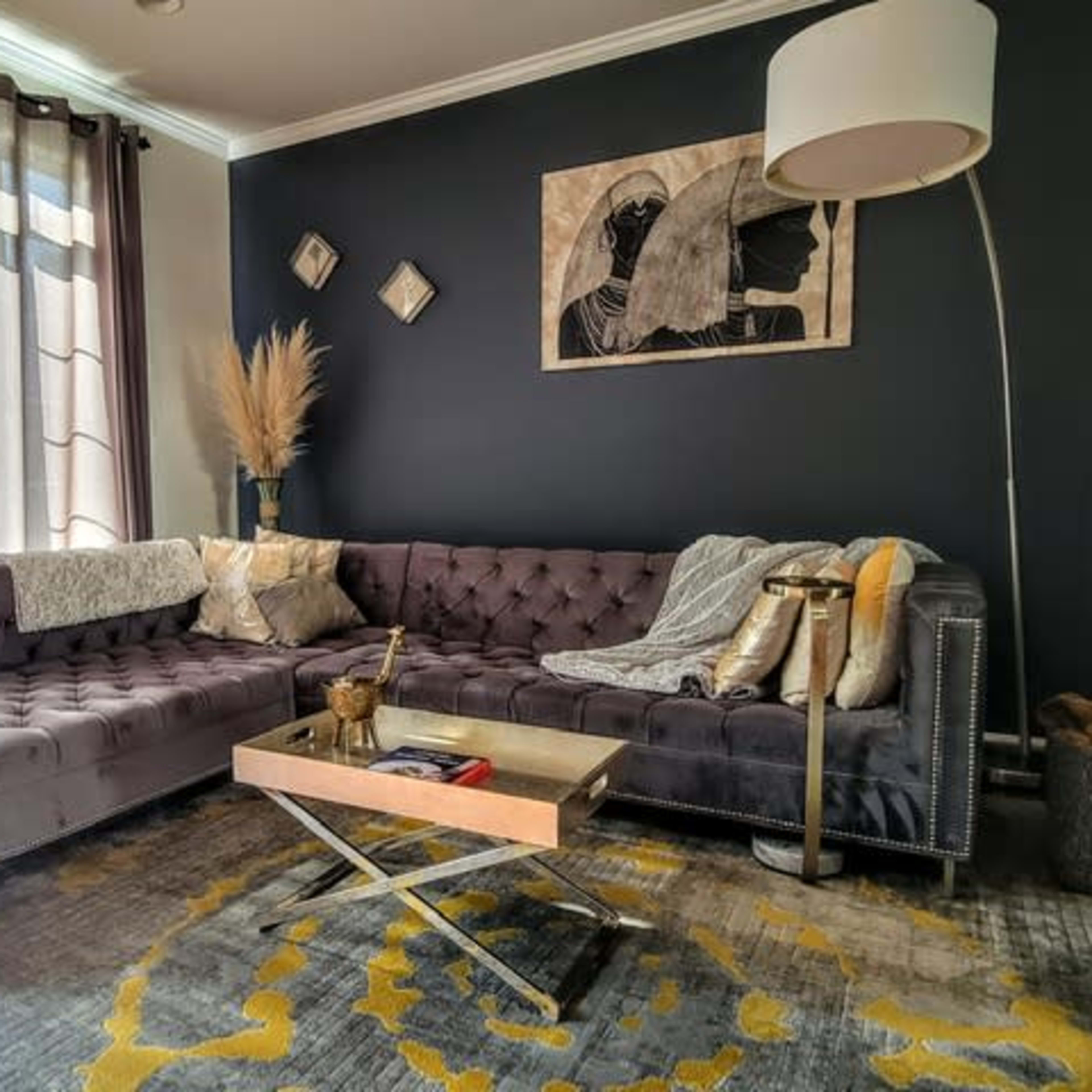 A modern living room features a dark wall, a plush sectional sofa with cushions, a coffee table, and decorative elements like plants and artwork.