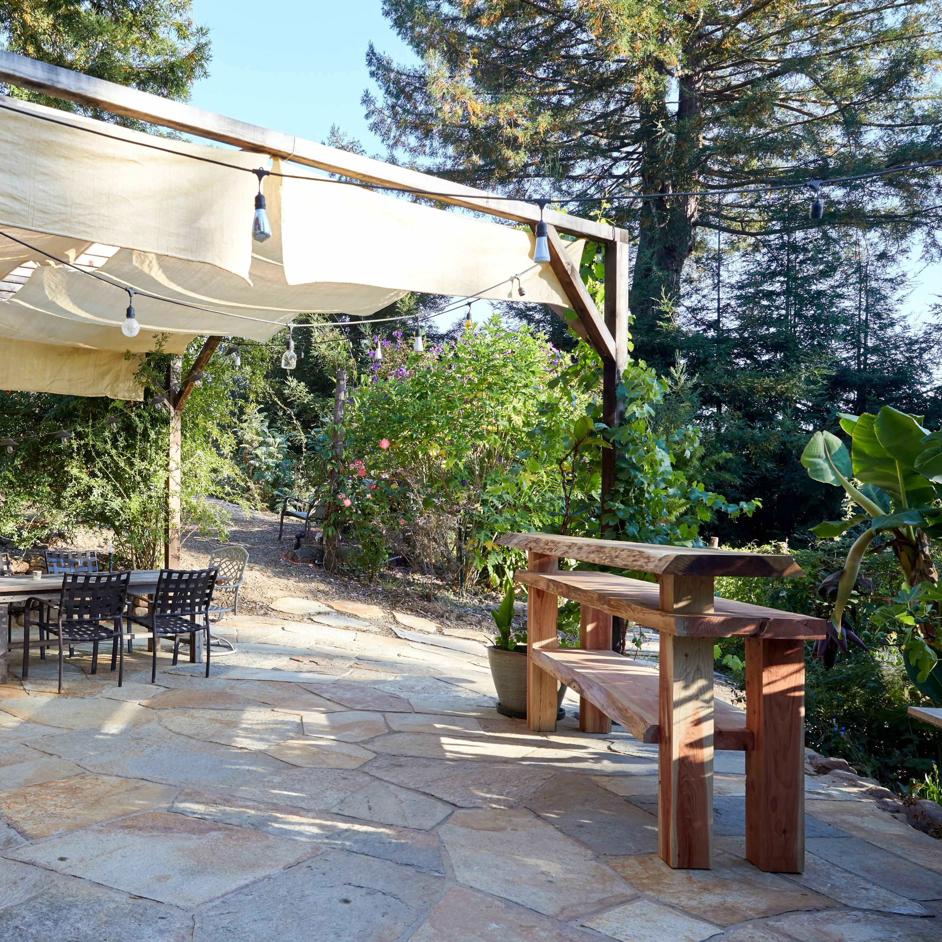 A patio area features wooden tables and chairs under a canopy, surrounded by greenery.