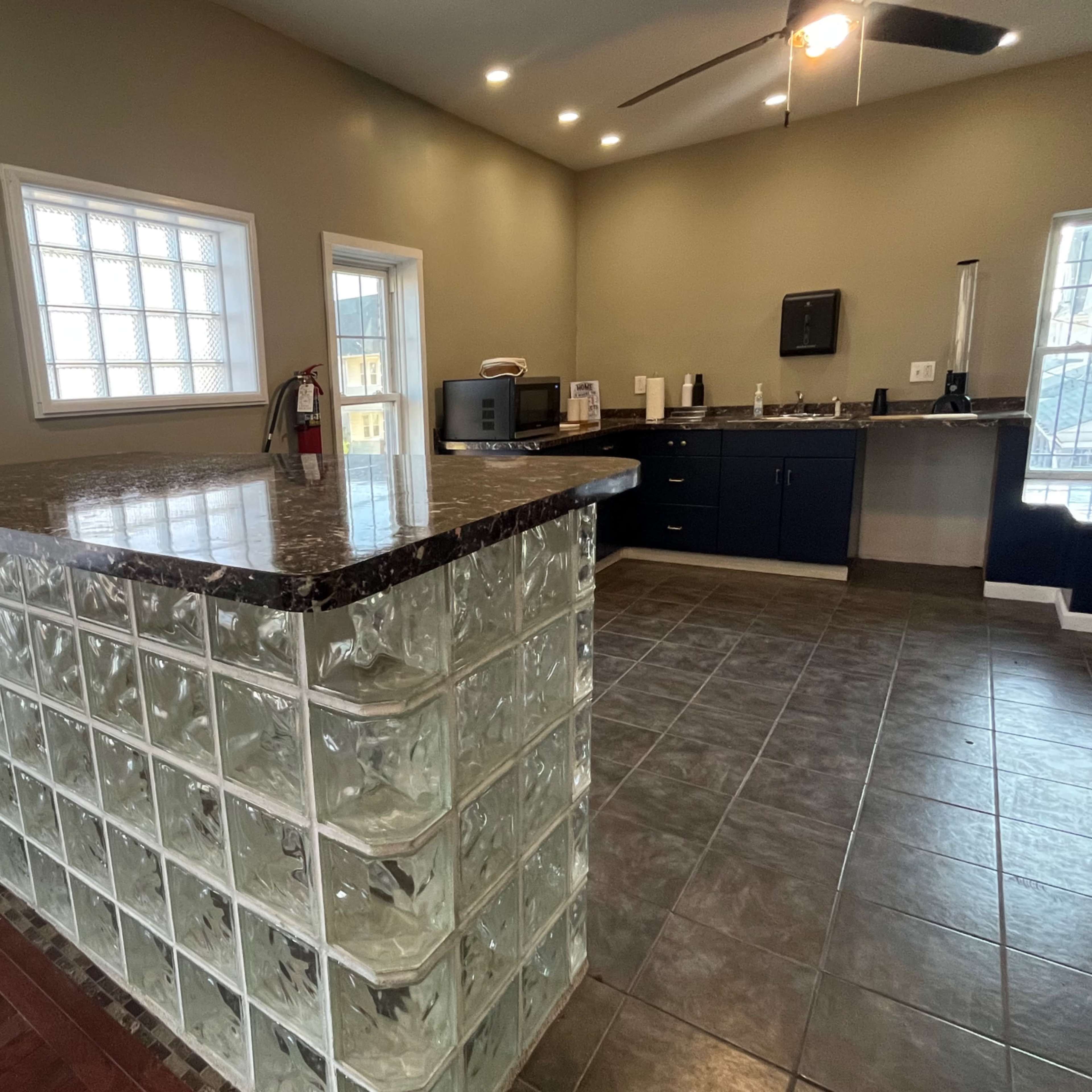 A modern kitchen with a large granite countertop and a glass block partition separating the cooking area from a dining space.
