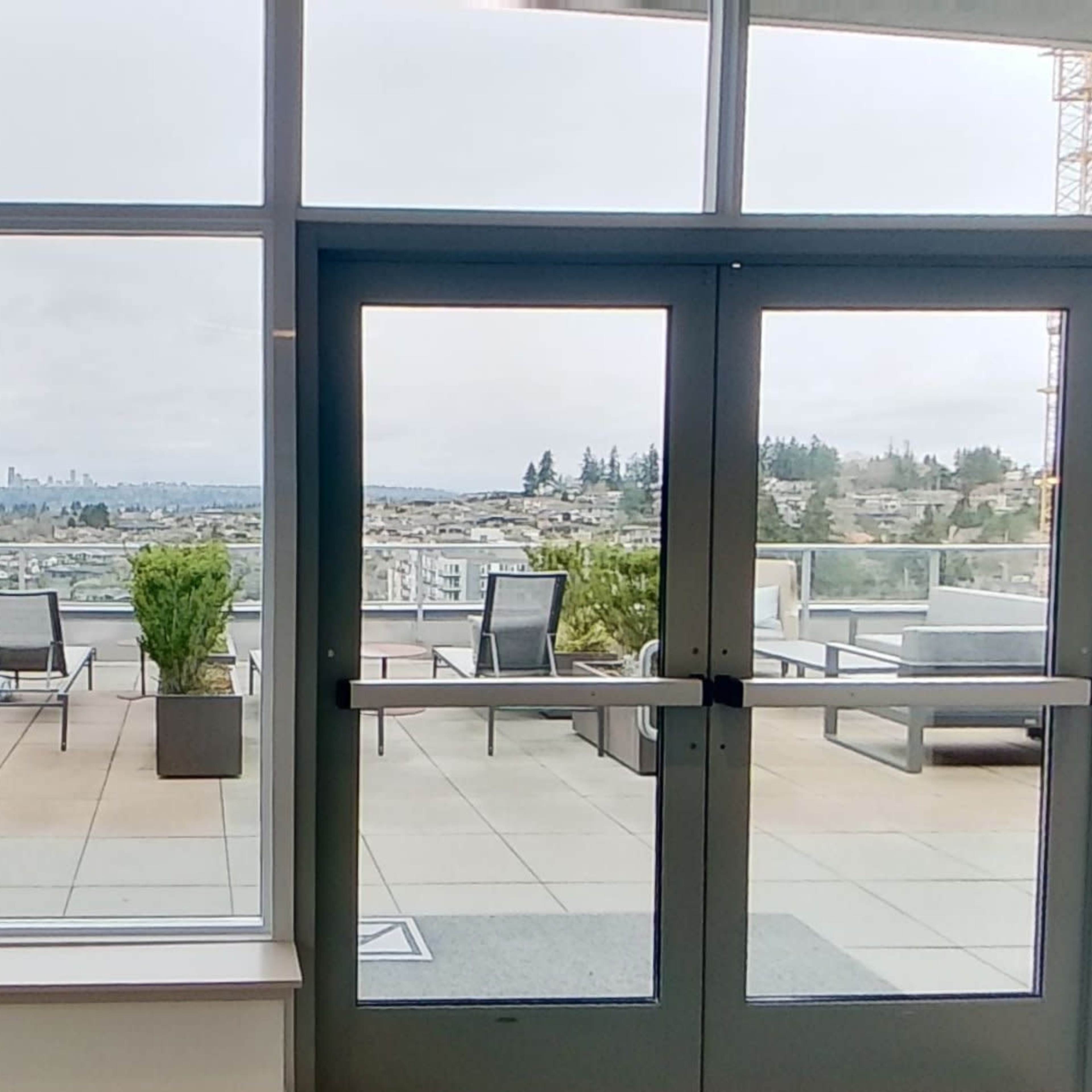 A pair of glass doors open to a patio area with seating and a view of the landscape in the distance.