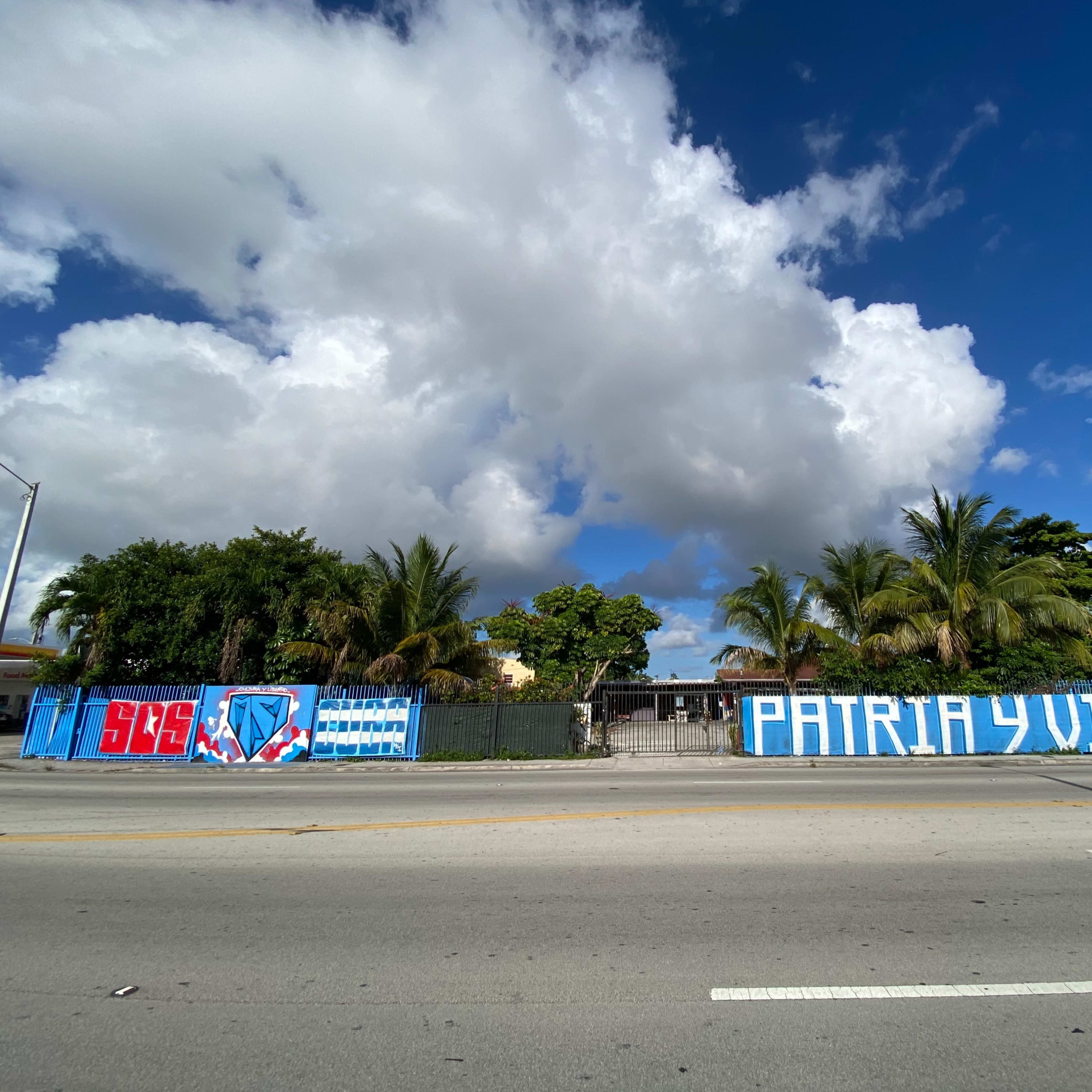 A building surrounded by palm trees with large blue and white murals displaying the phrases "SBS" and "PATRIA Y VIDA" on the walls.