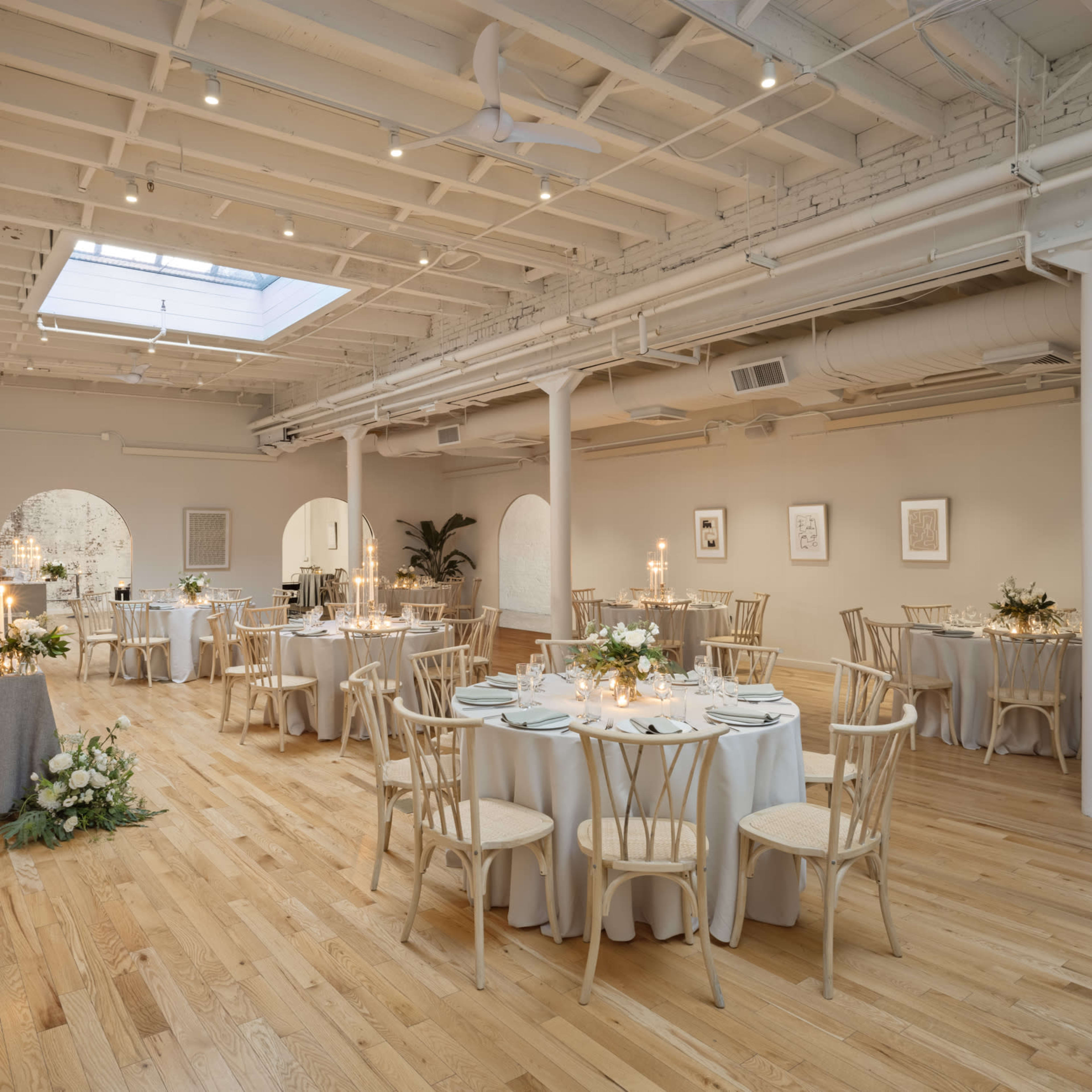 A spacious event venue with wooden floors, tables set for dining, and large windows providing natural light.
