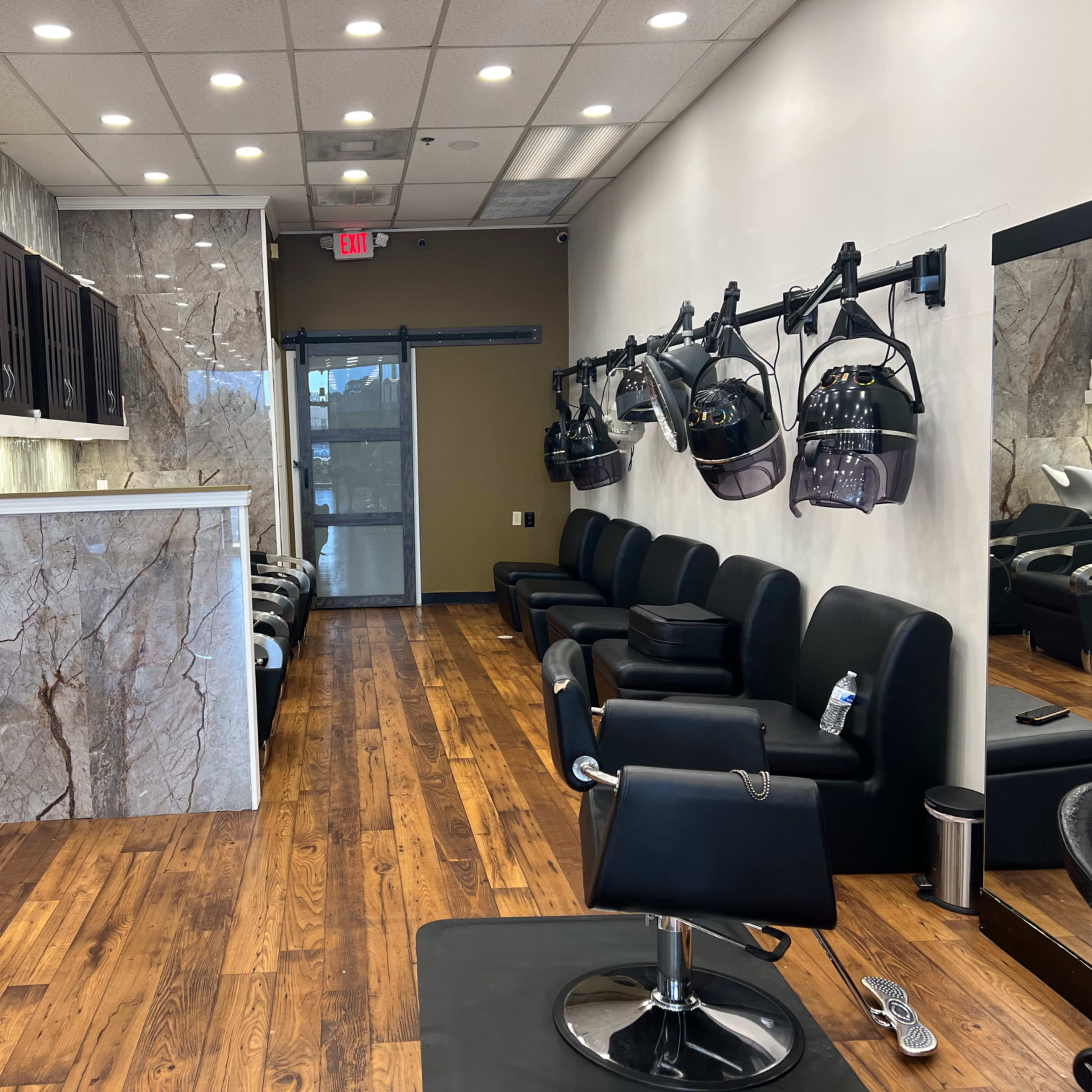 A modern hair salon interior with black chairs, a marble reception area, and hairdryer stations mounted on the wall.