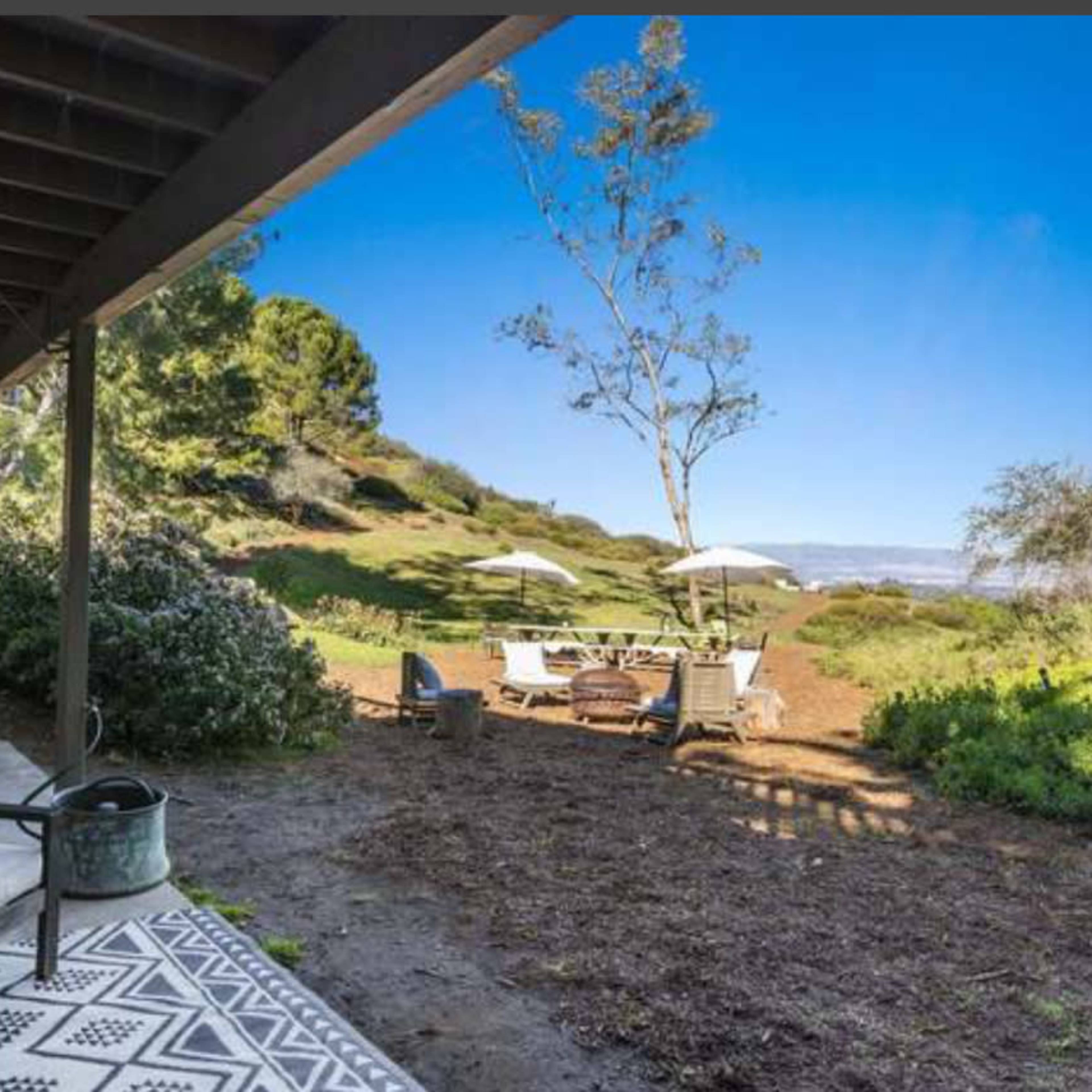 A patio area with seating overlooks a grassy hillside featuring outdoor tables and umbrellas.