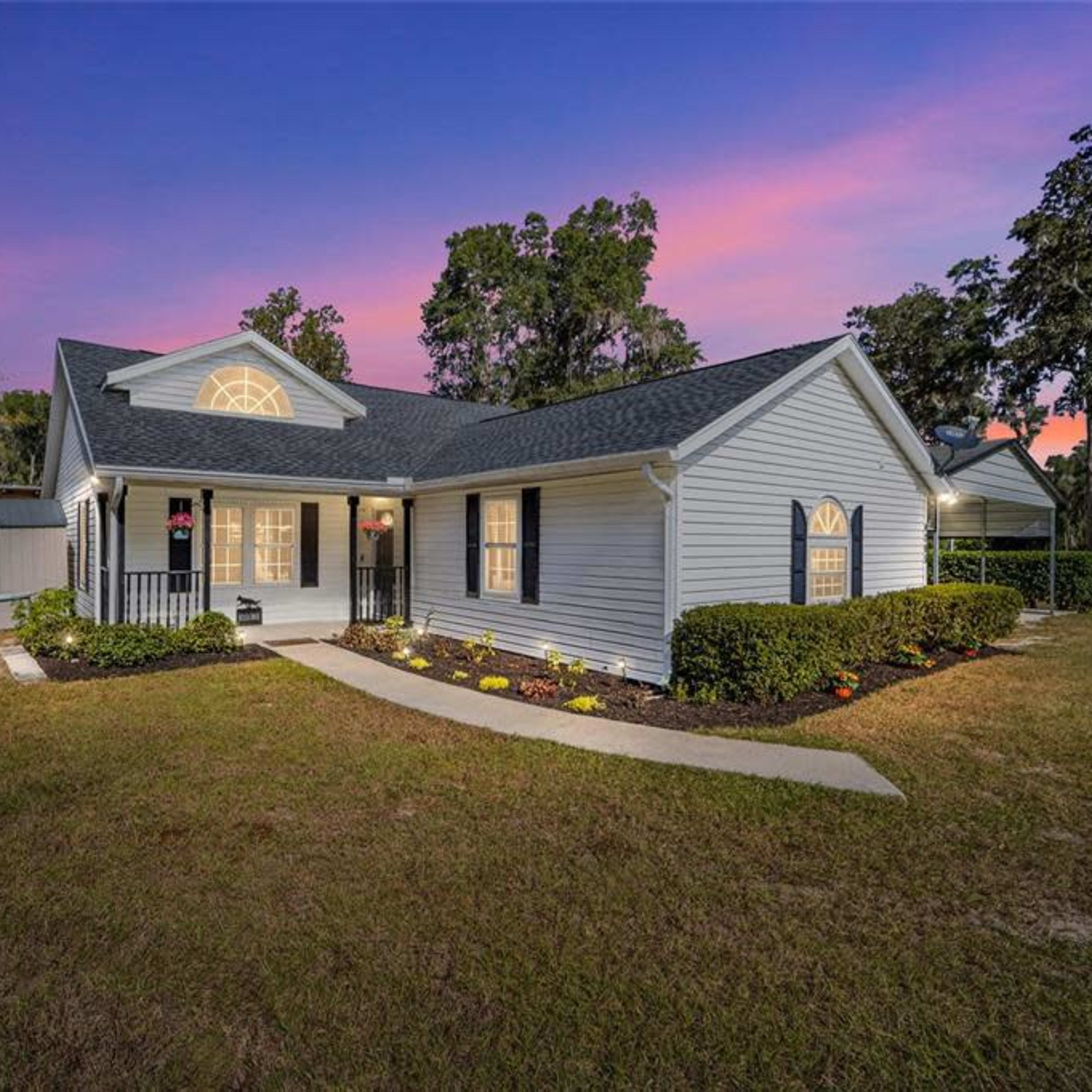 A single-story house with a landscaped front yard, situated under a colorful twilight sky.