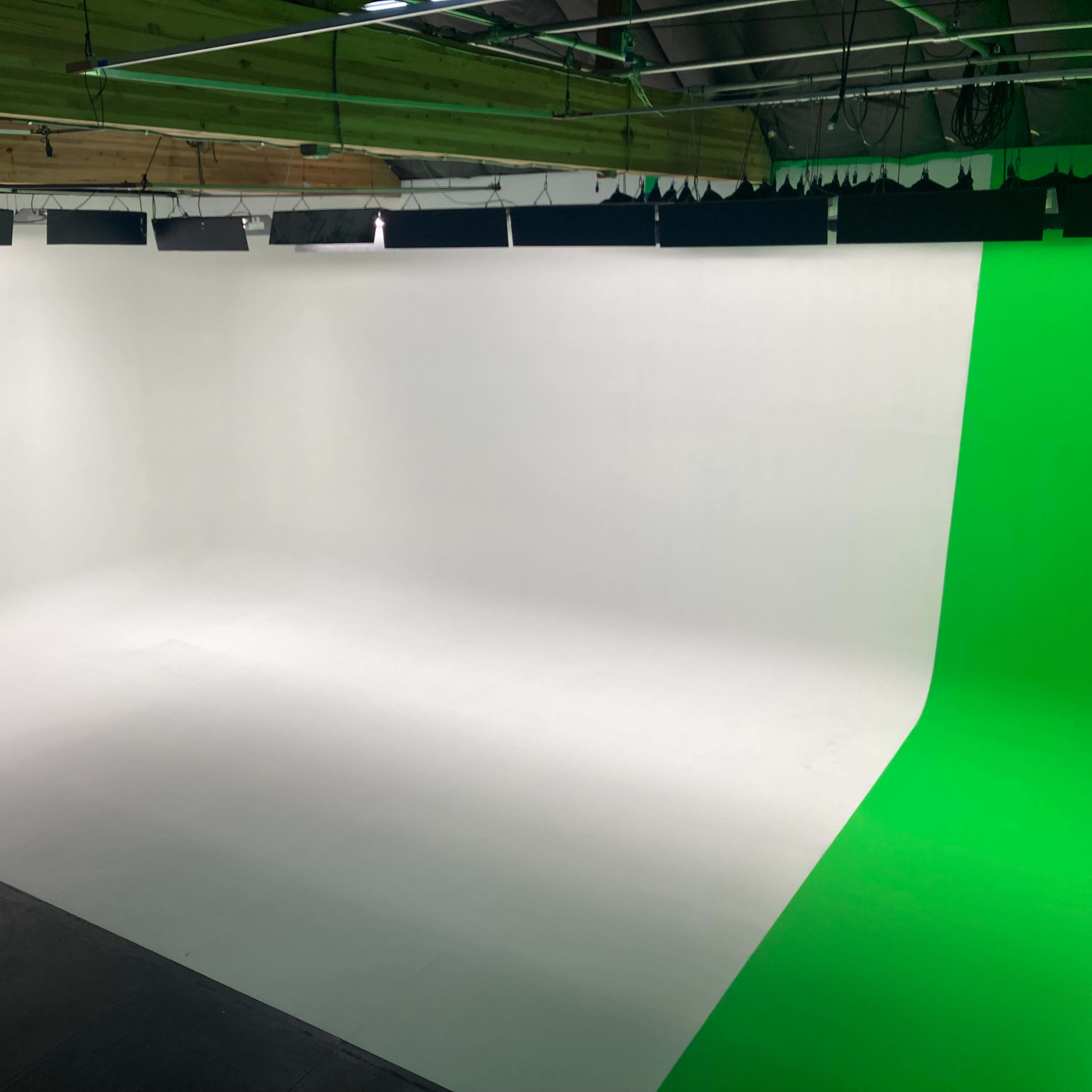 A photography studio with a white backdrop on one side and a green screen on the other.