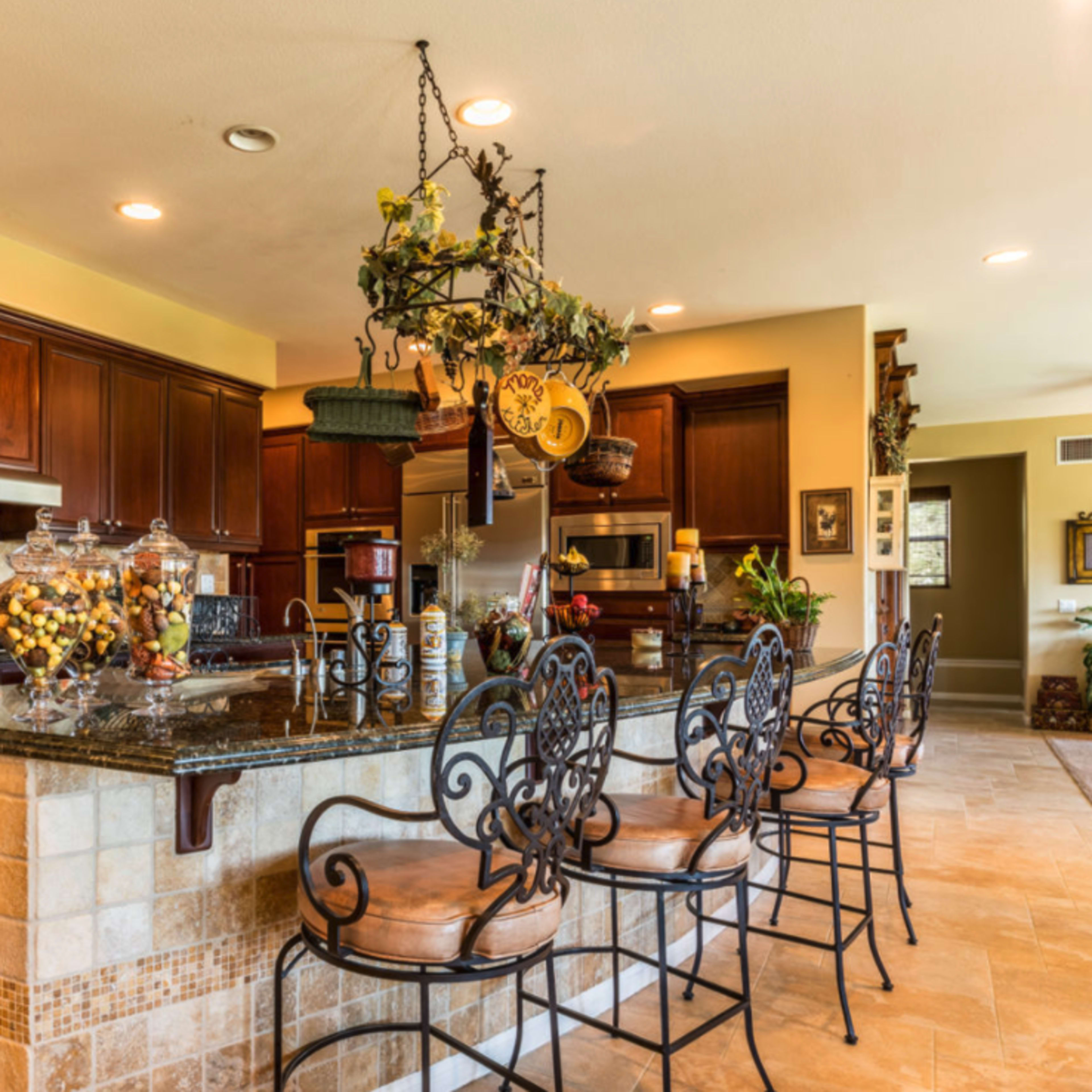 A spacious kitchen with wooden cabinets, a granite countertop, and several bar stools arranged along the island.