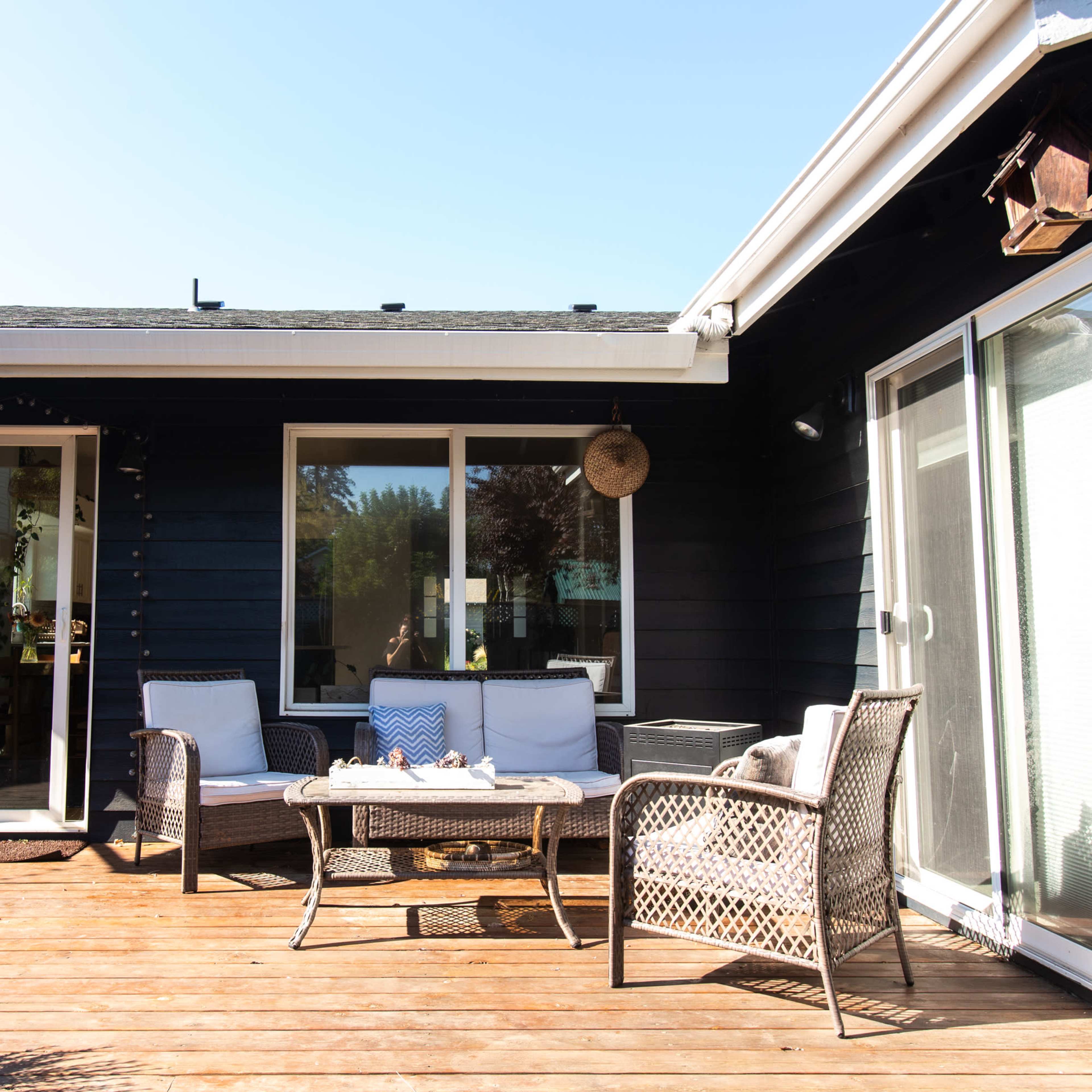 A deck with a wicker seating set and a small table in front of a house with a dark exterior.