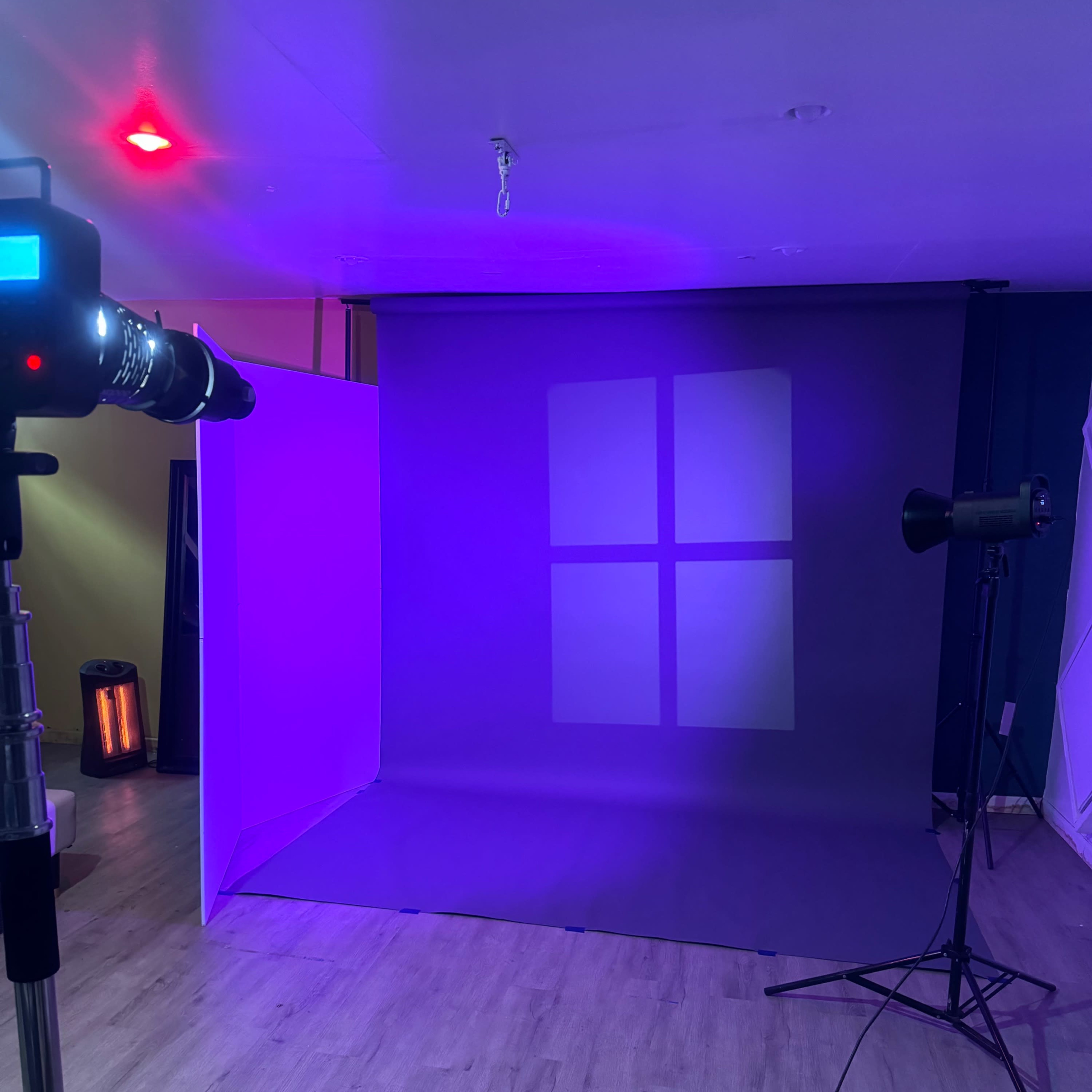 A photography studio setup featuring a backdrop with soft lighting, a camera on a tripod, and a spotlight positioned on the side.