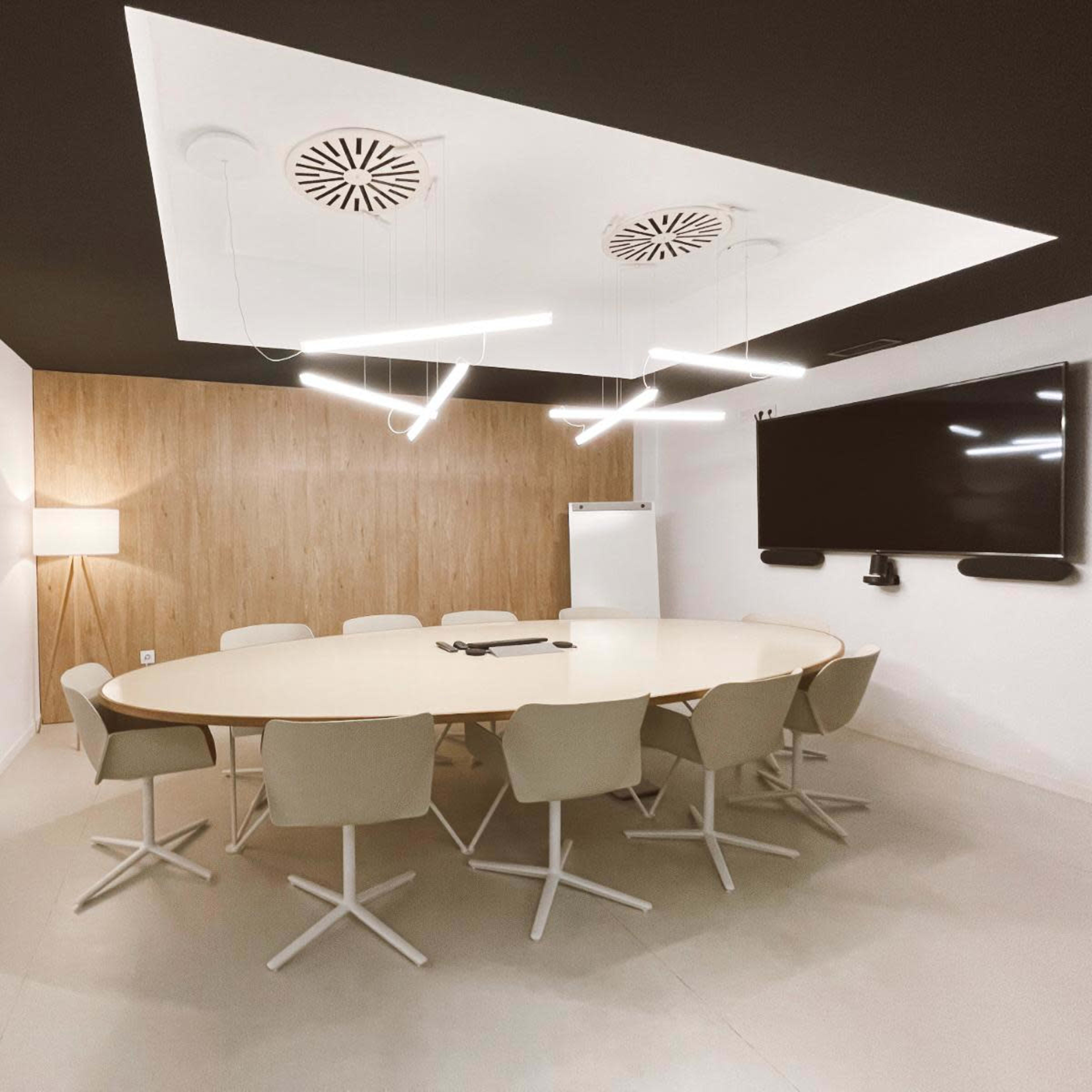A modern conference room features a circular table surrounded by light-colored chairs, a wall-mounted television, and contemporary lighting.