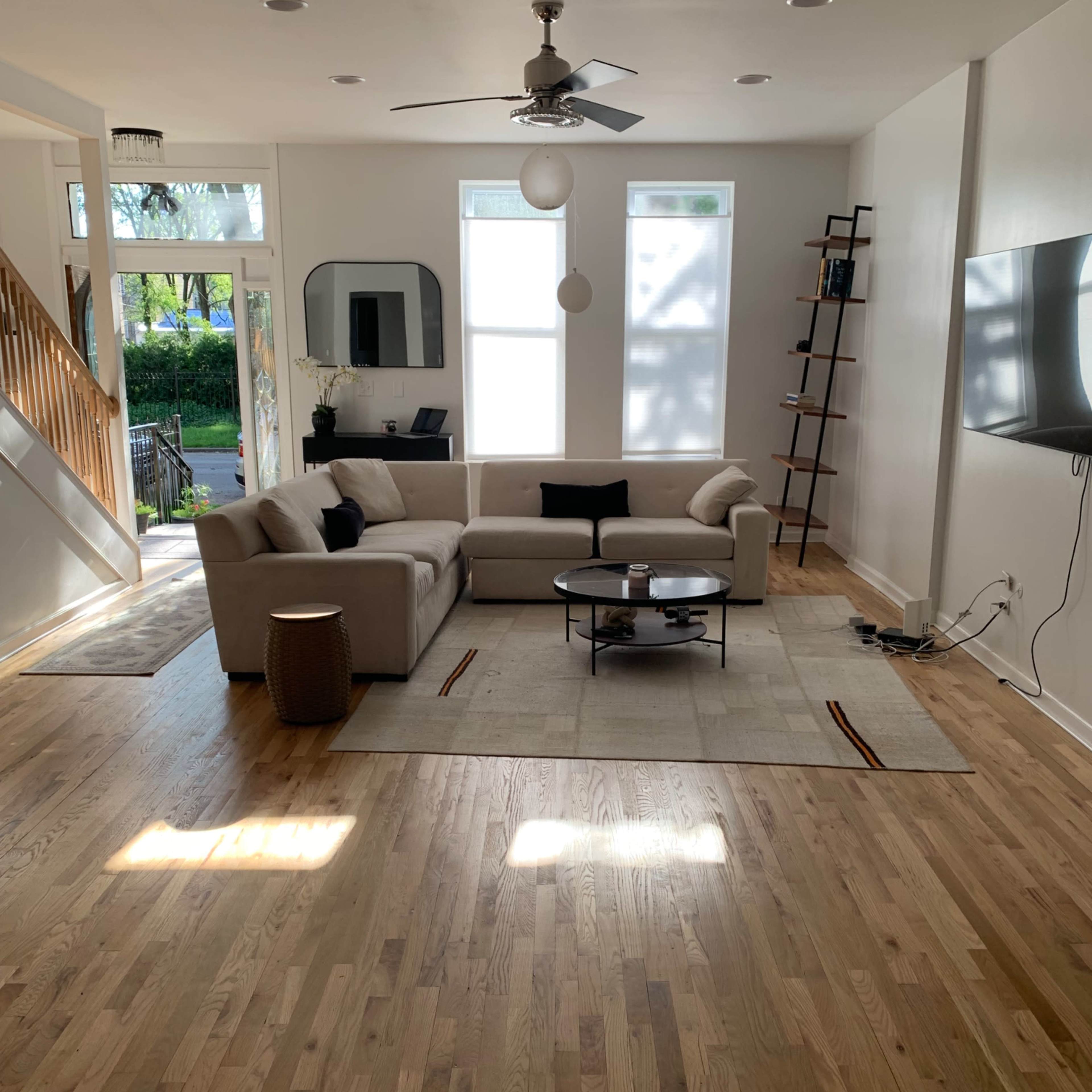 A modern living room with a light-colored sofa, a coffee table, and large windows allowing natural light to enter.