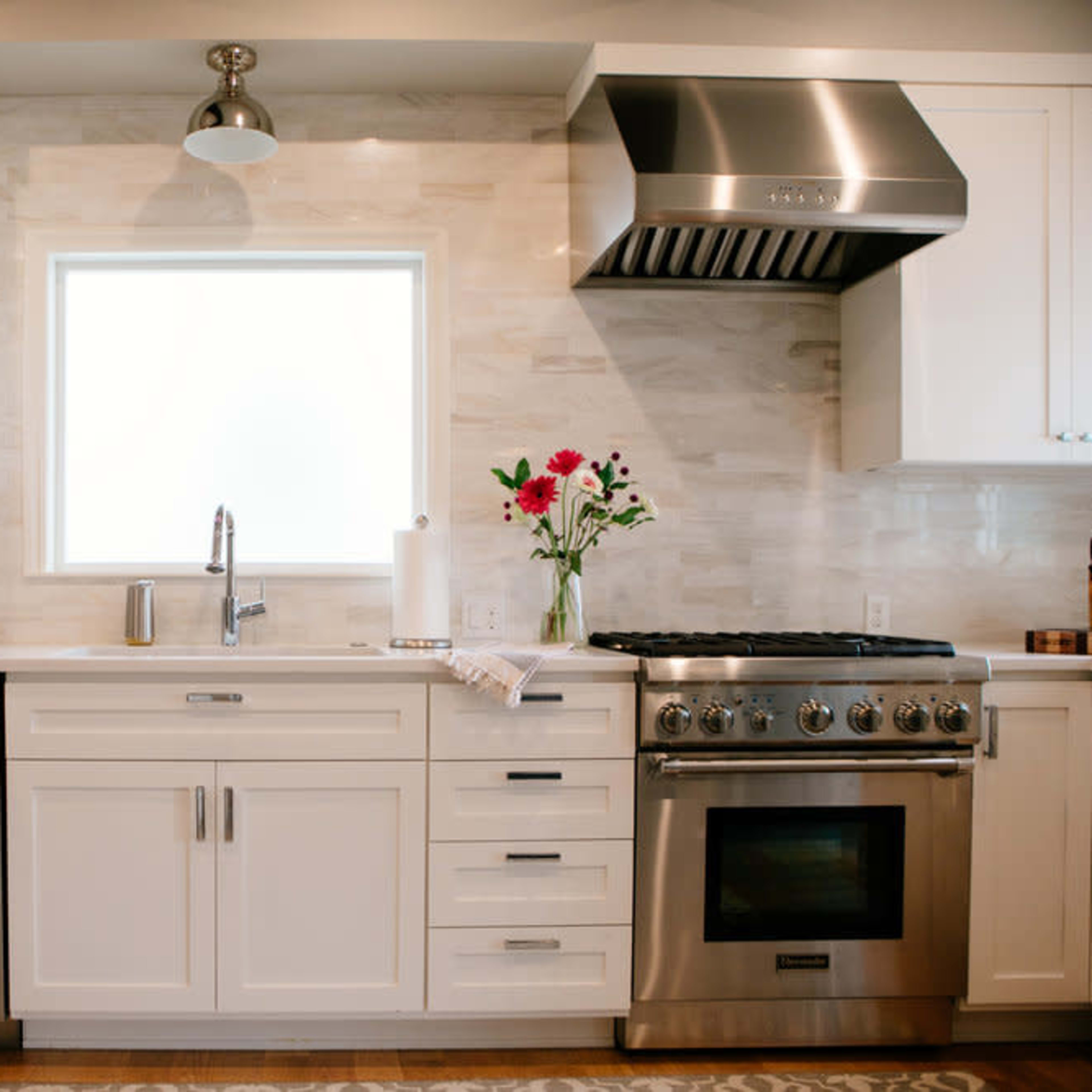 A modern kitchen with white cabinets, a stainless steel refrigerator and oven, and a window above the sink.