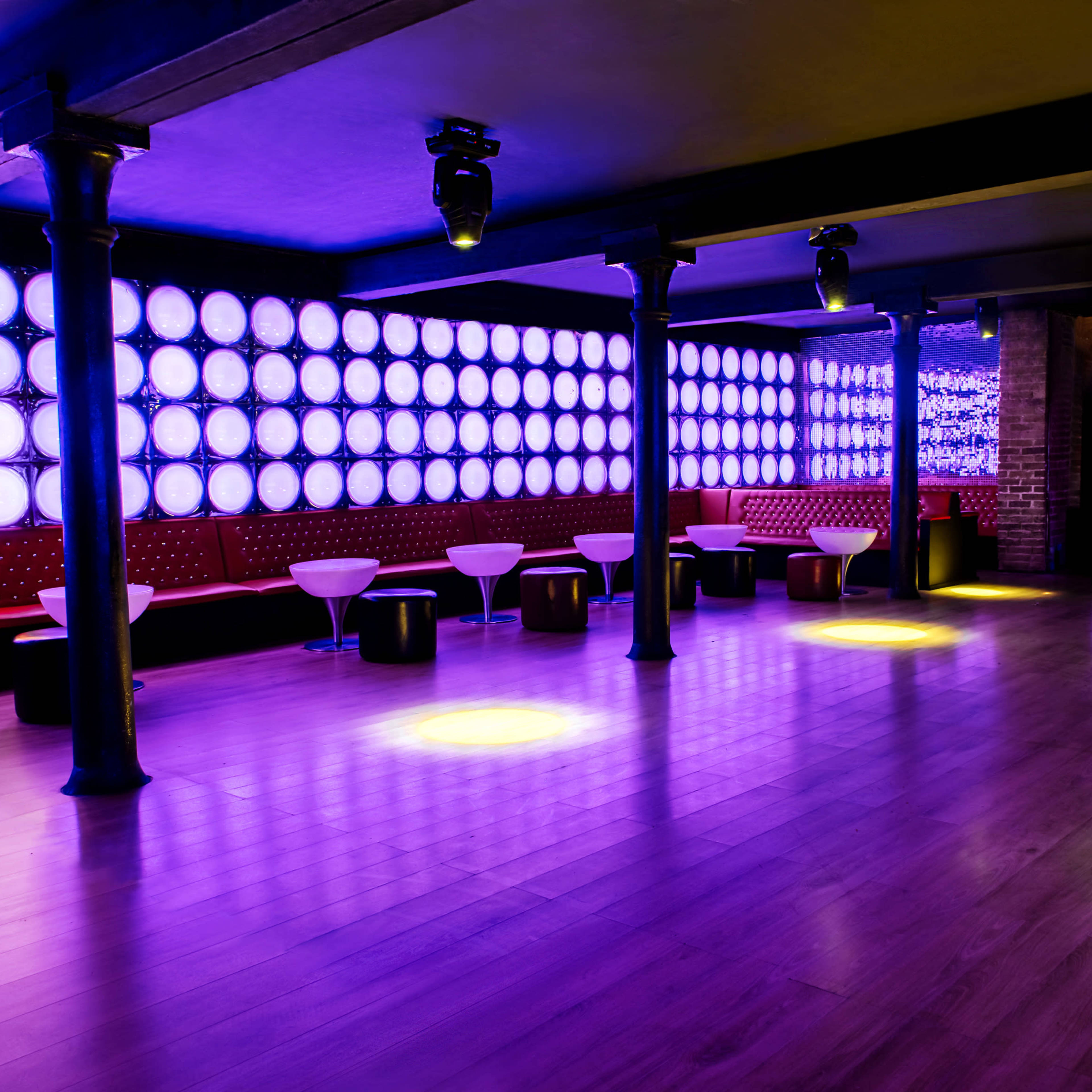 A spacious nightclub interior features illuminated walls and circular seating arrangements under soft lighting.