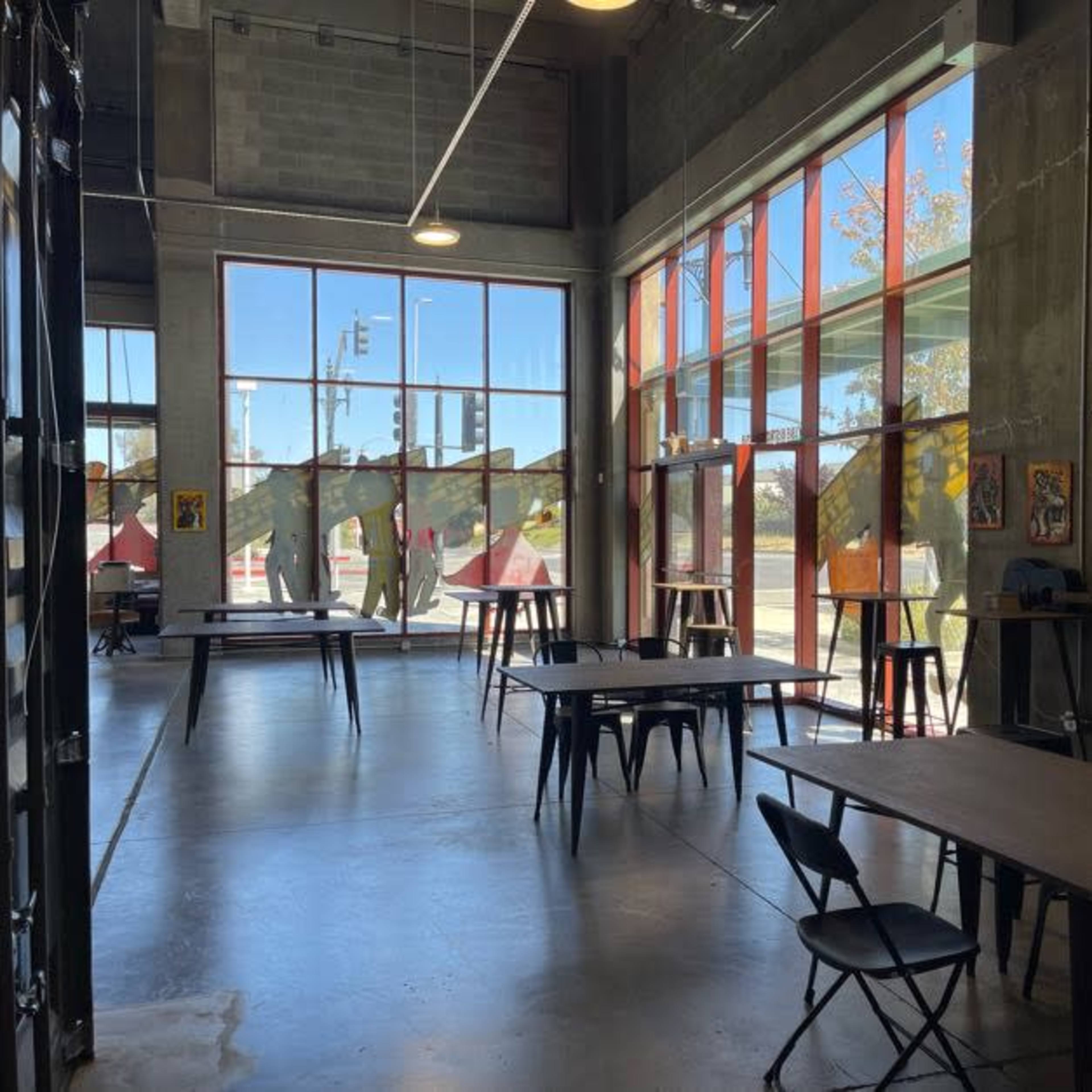 A spacious room with large windows, concrete walls, and several tables and chairs arranged for use.