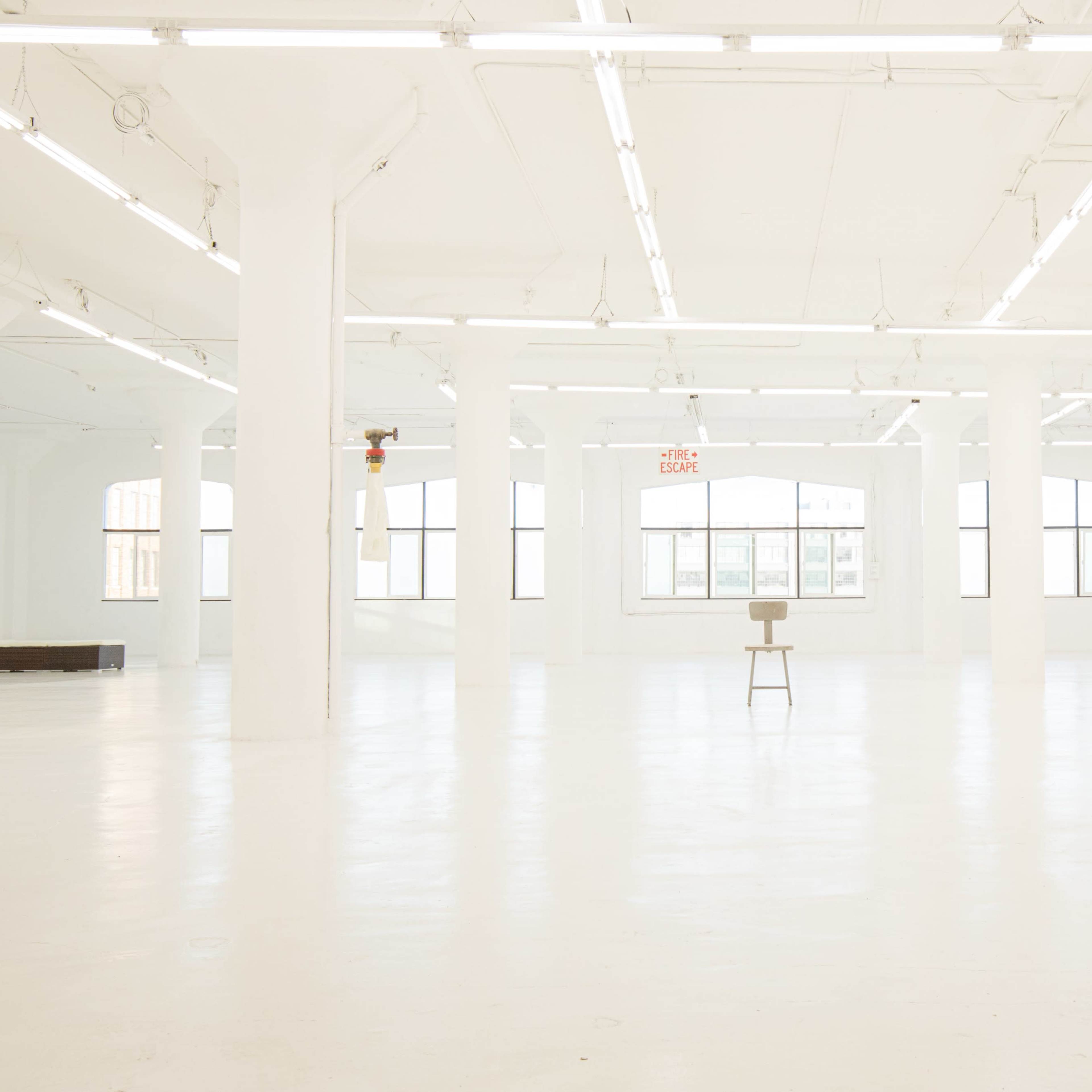 A spacious, well-lit white room with tall pillars and a single stool in the center.