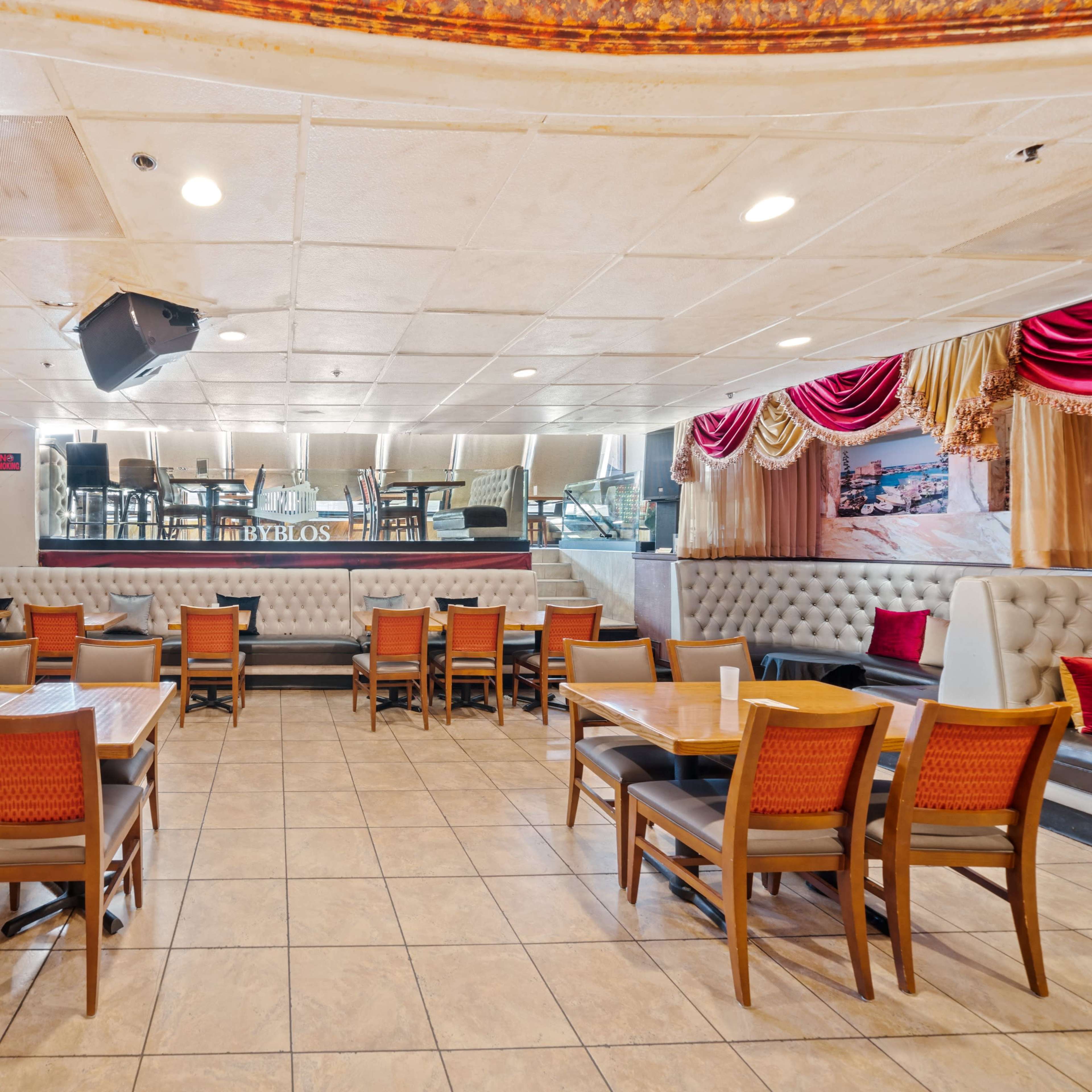 An interior view of a restaurant, featuring several tables and chairs arranged in a spacious layout, with a stage and sound equipment visible at the back.