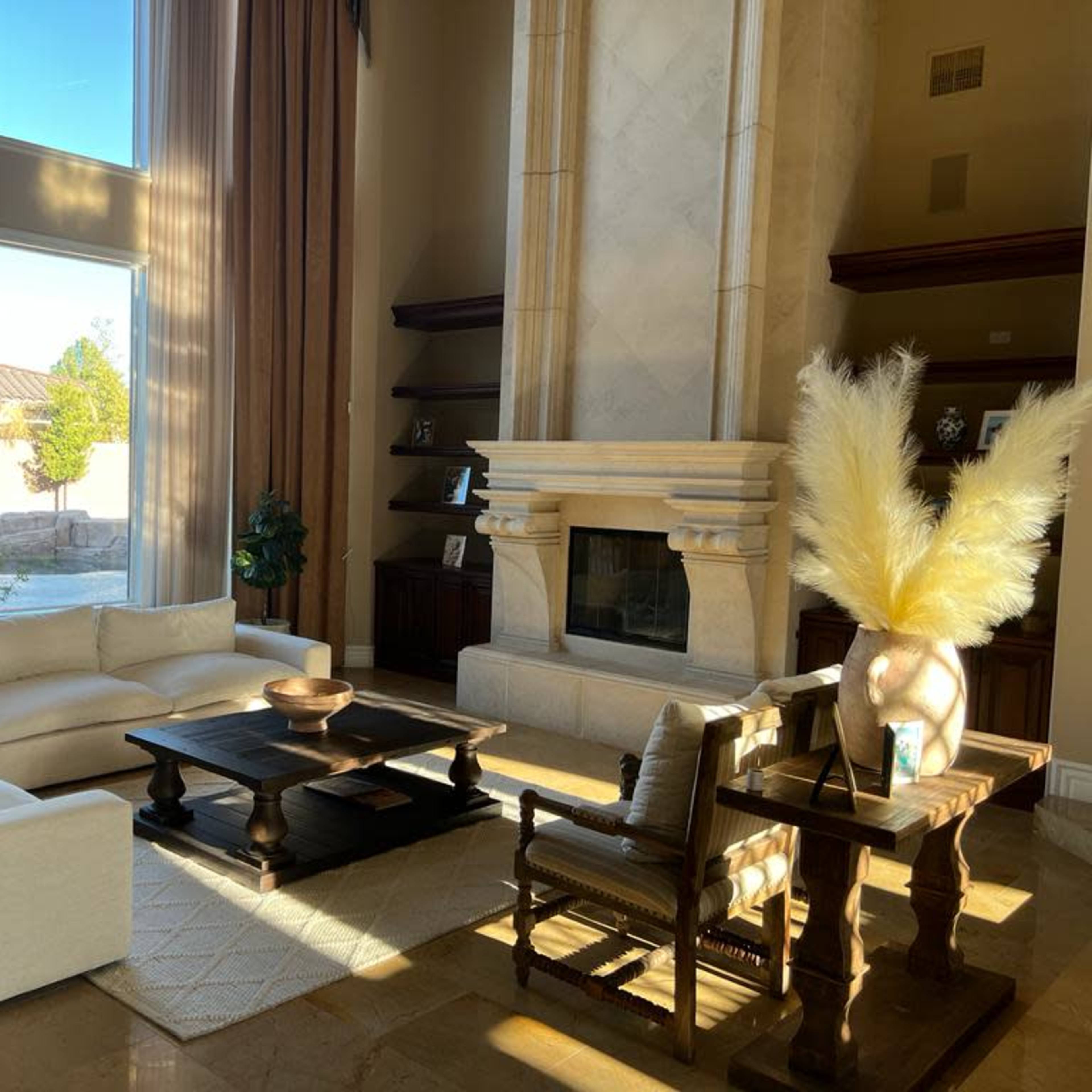 A spacious living room with large windows, a fireplace, and modern furniture arranged around a wooden coffee table.