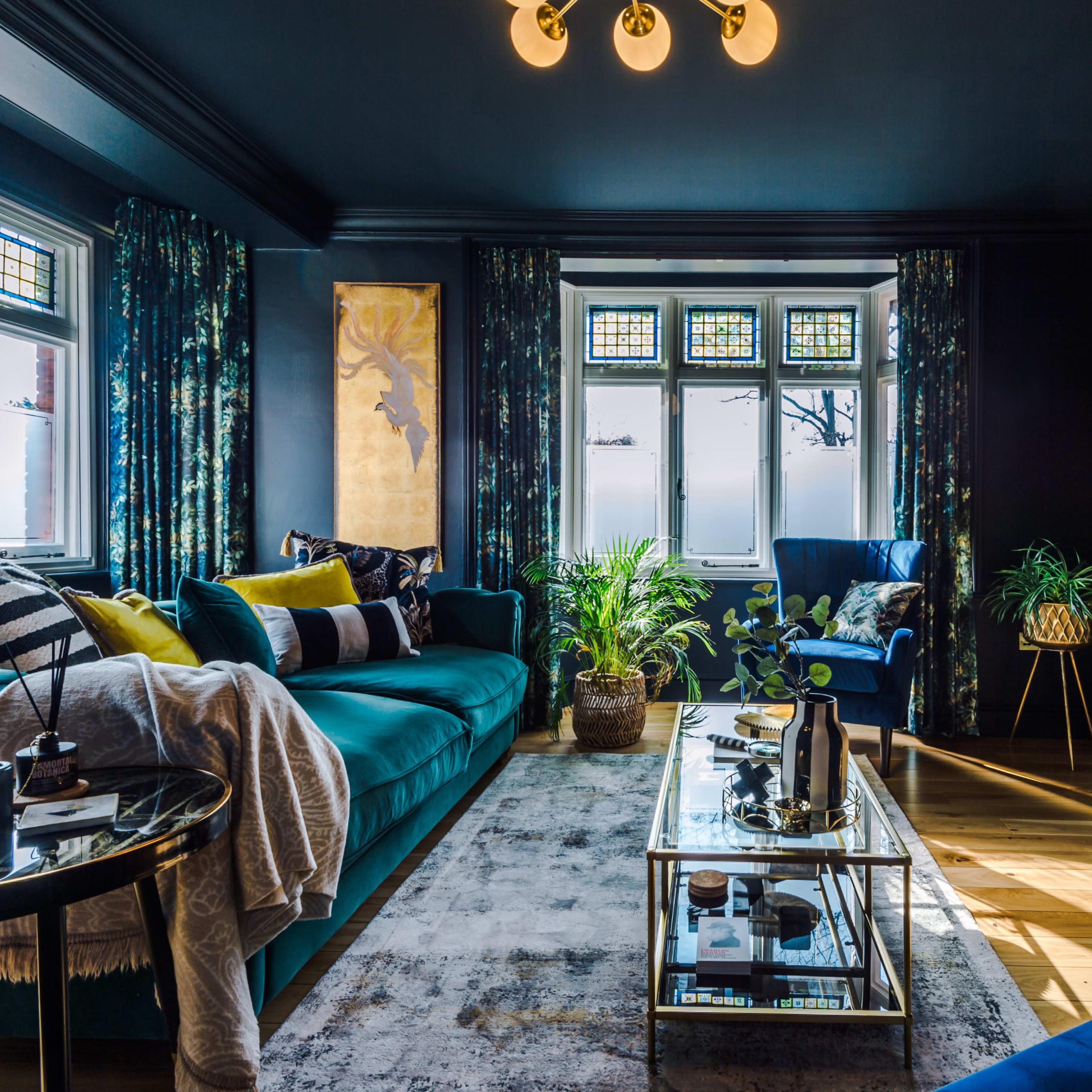 A modern living room featuring a deep blue sofa, a glass coffee table, and large windows adorned with patterned curtains.