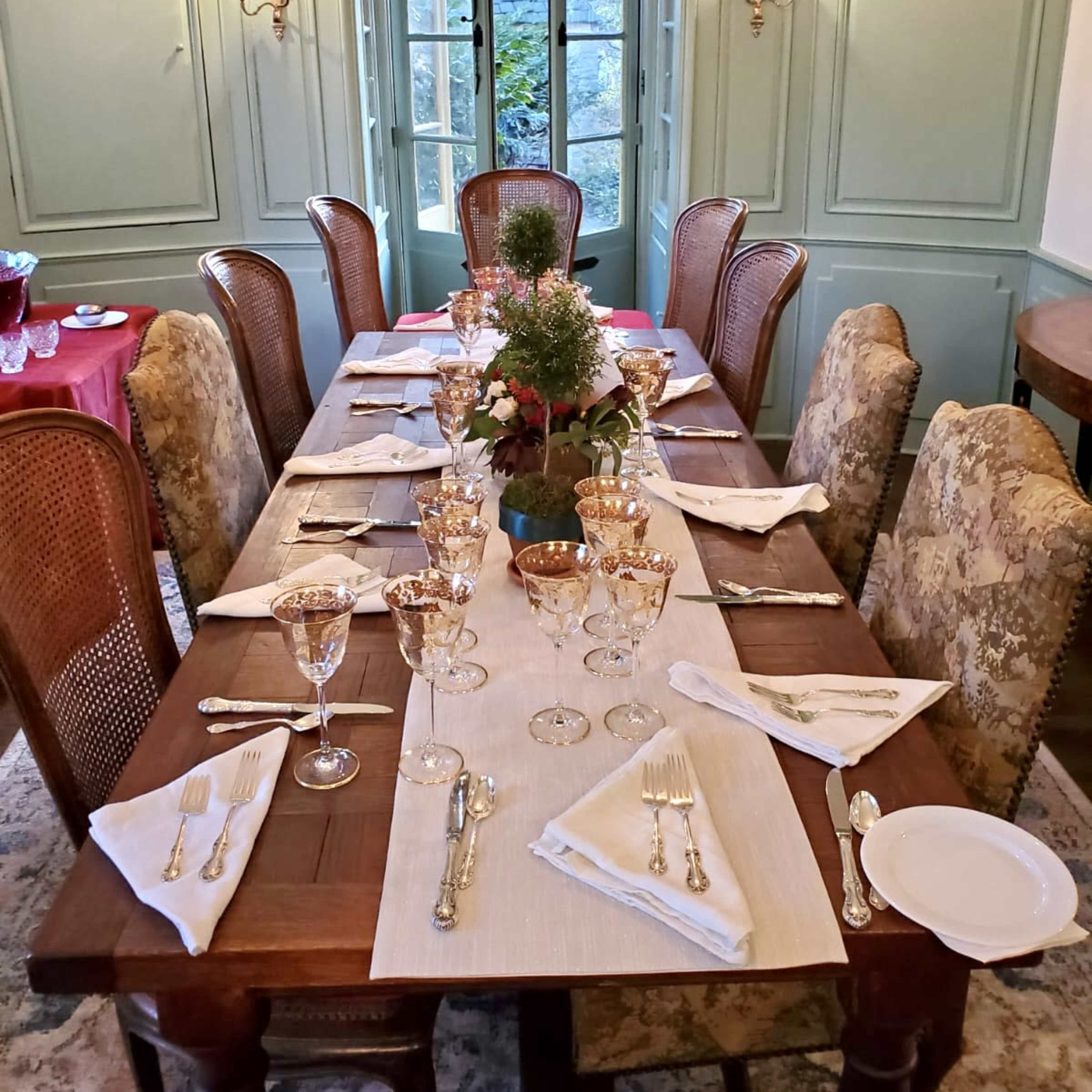 A formal dining room features a long wooden table set with elegant glassware and silverware, surrounded by upholstered chairs.