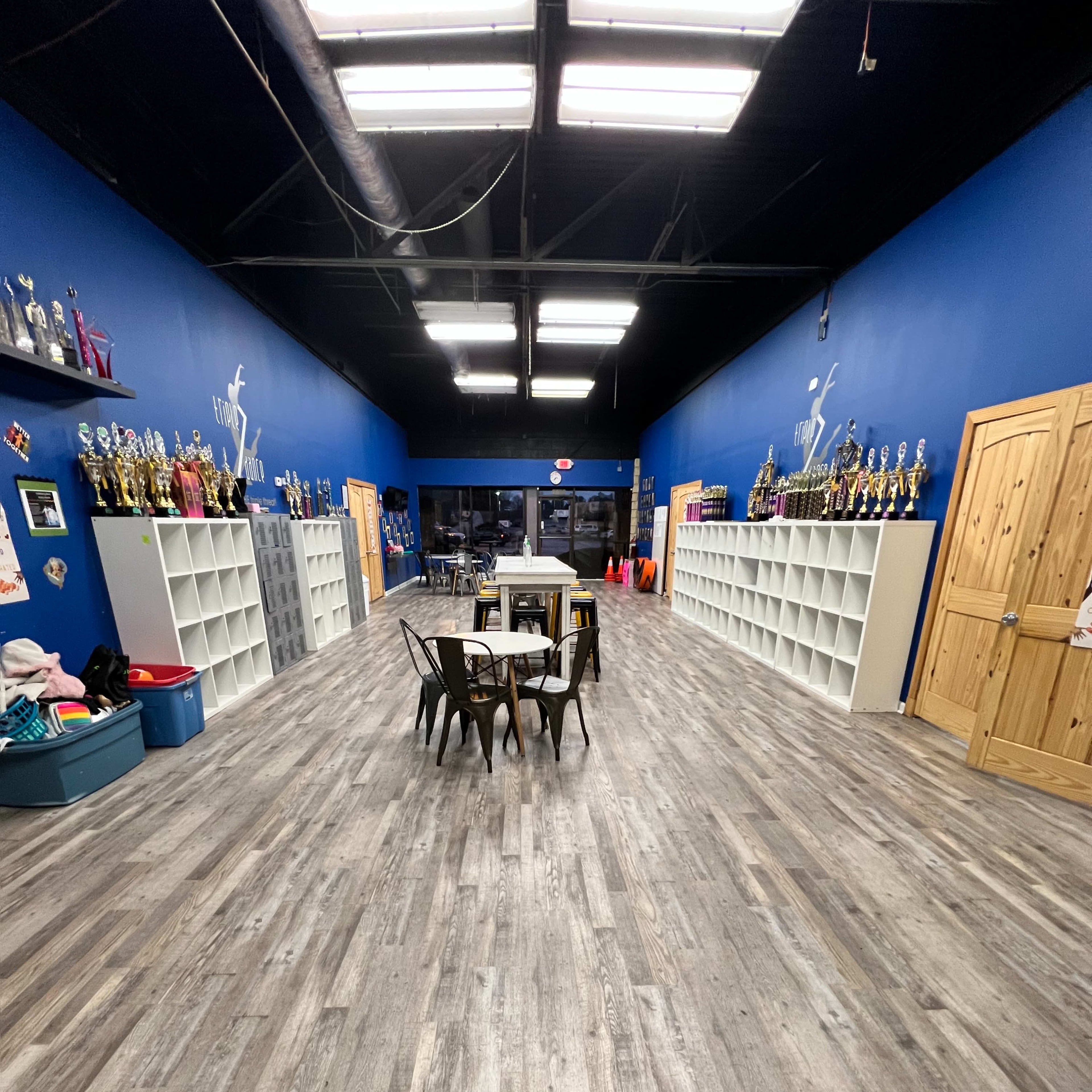 A long, narrow room with blue walls, shelves filled with trophies along the sides, and a table with chairs in the center.