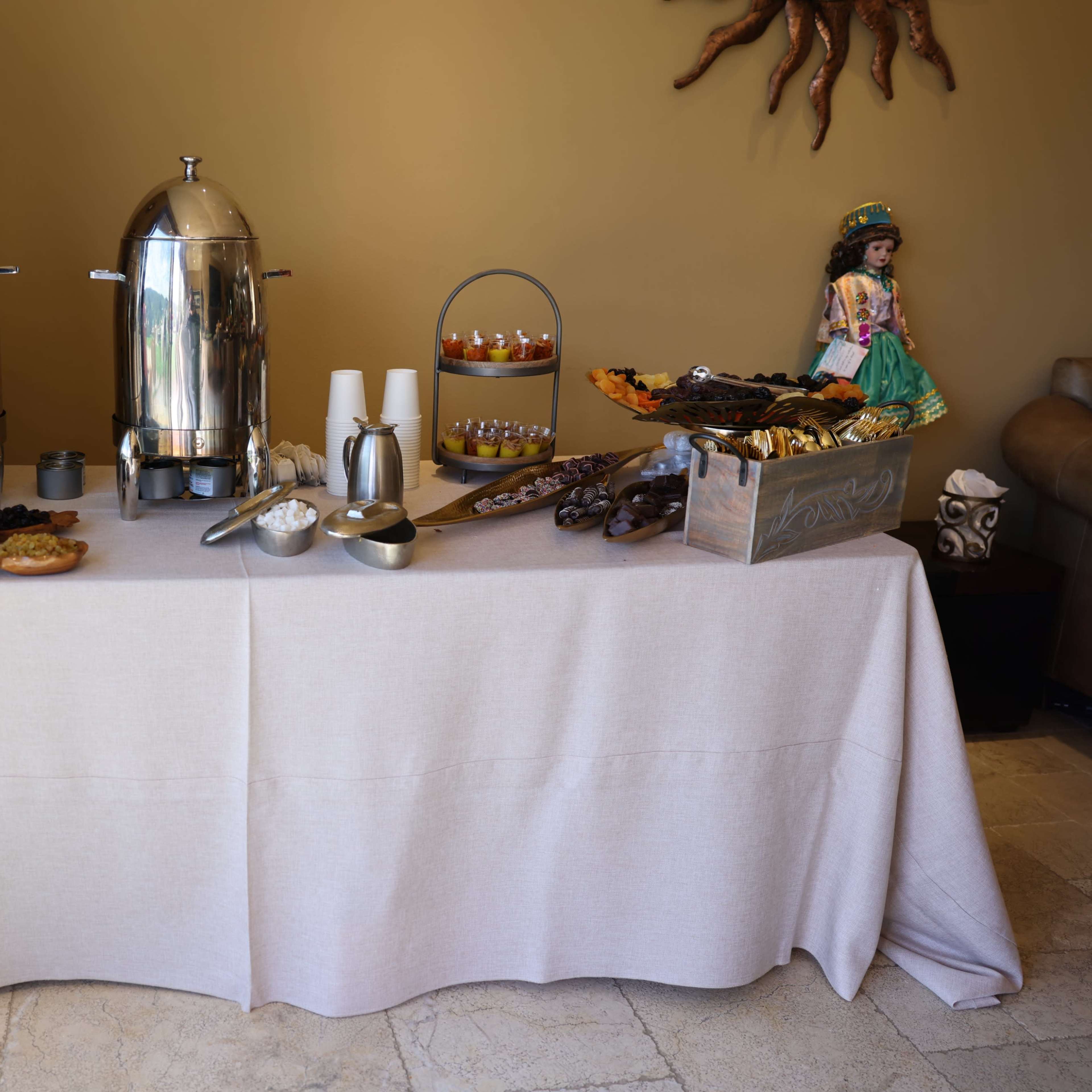 A table is set with two silver beverage dispensers and an assortment of food items arranged on trays and platters.