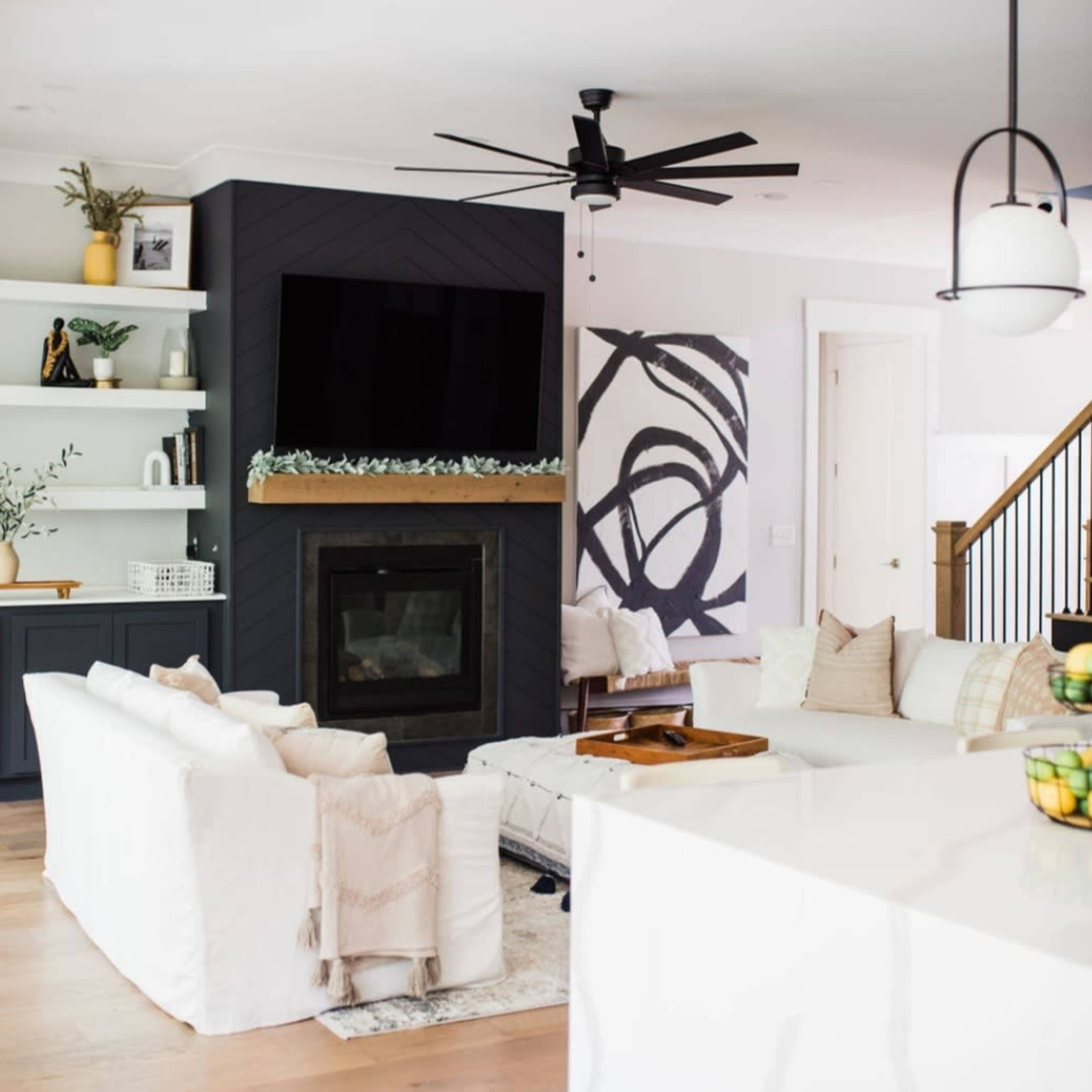 A modern living room featuring a black fireplace with a television above it, surrounded by white sofas and light wood flooring.