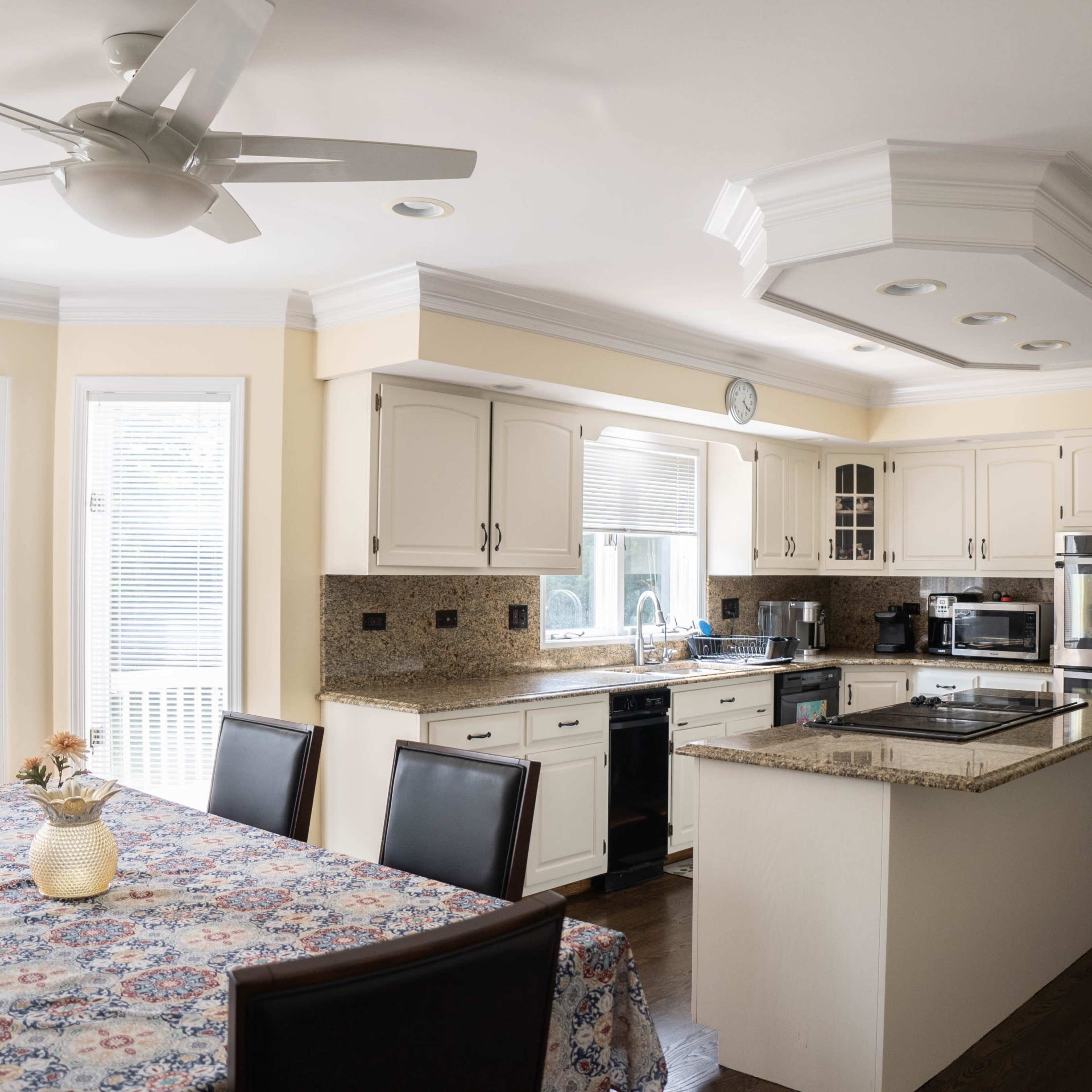 A bright kitchen featuring a central island, stainless steel appliances, and a dining table set with a floral tablecloth.