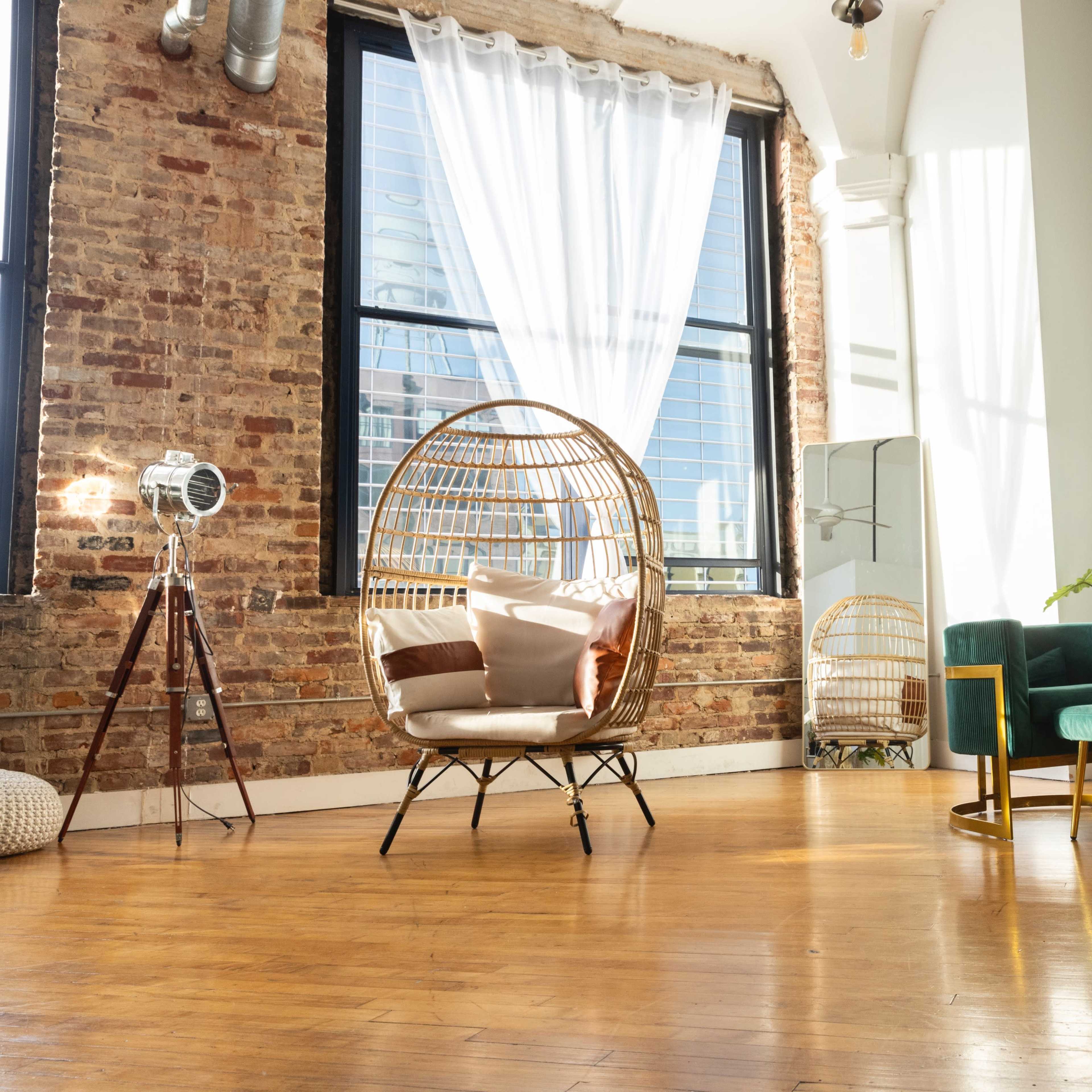 A bright, airy room featuring a rattan hanging chair, a teal sofa, and a coffee table on polished wooden flooring, with large windows letting in natural light.