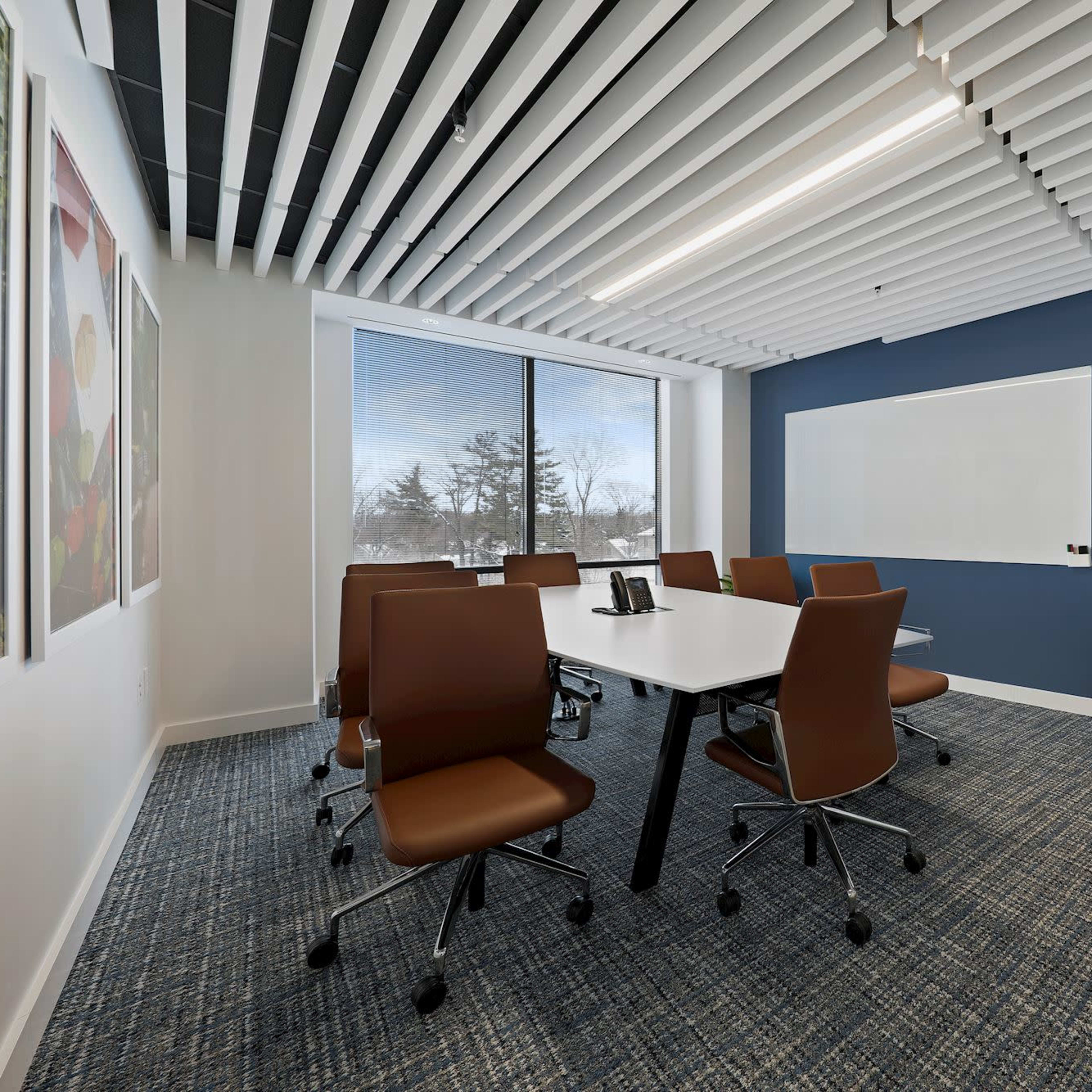 A modern conference room features a large table, ergonomic chairs, a whiteboard, and a wall-mounted TV, with large windows providing natural light.