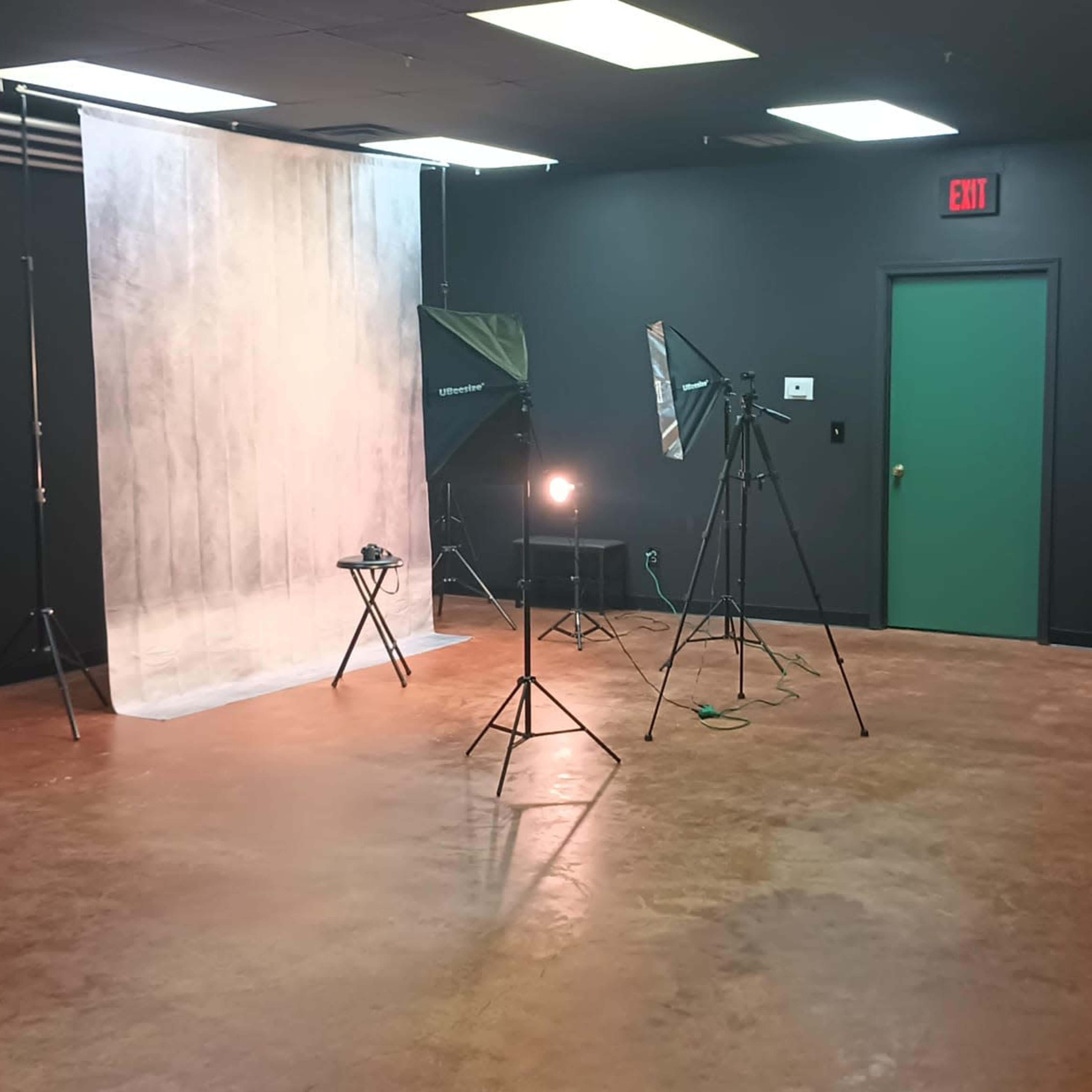 A photography studio with a backdrop, lighting equipment, and a green door.