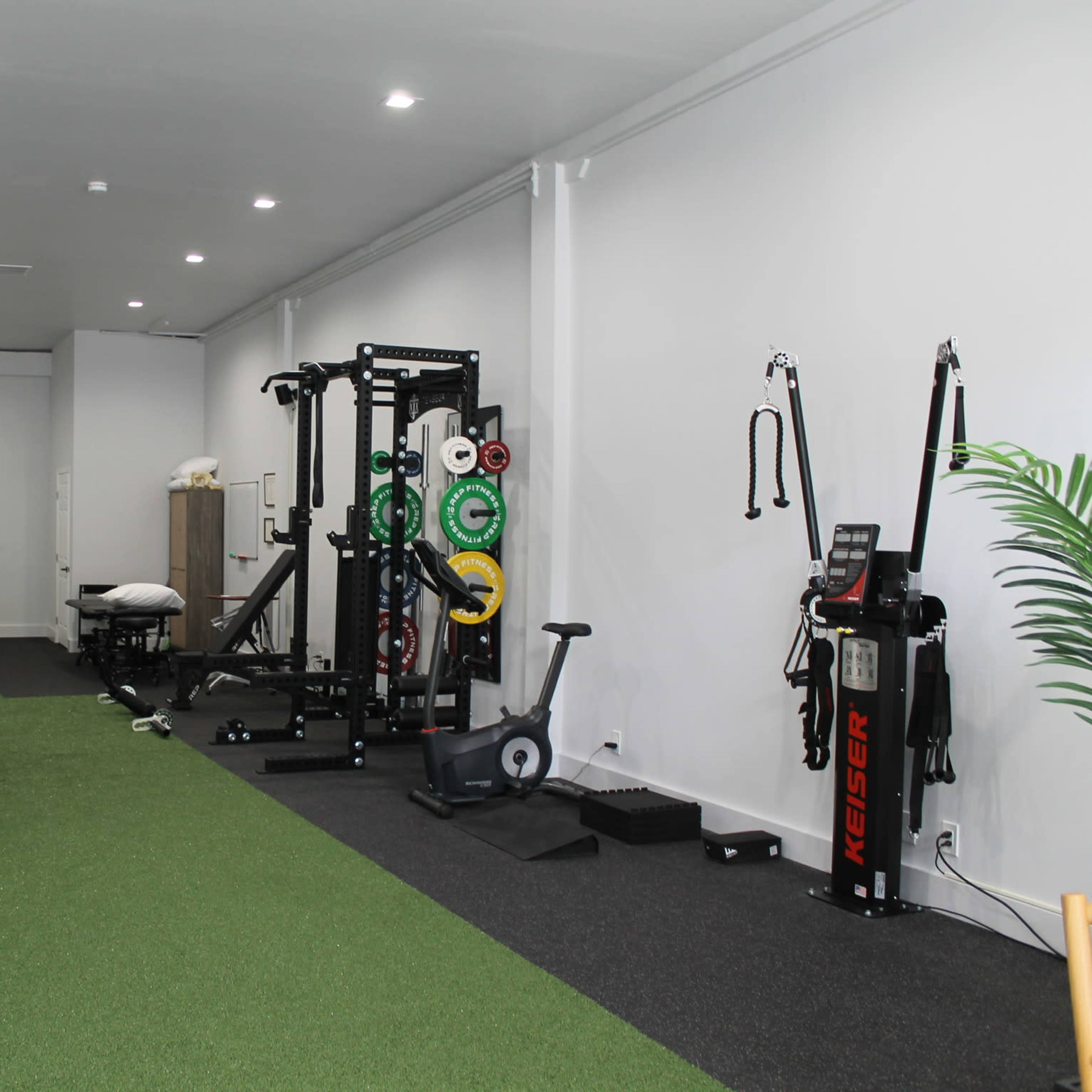 A modern gym interior with turf flooring, various workout equipment, and a spacious layout.