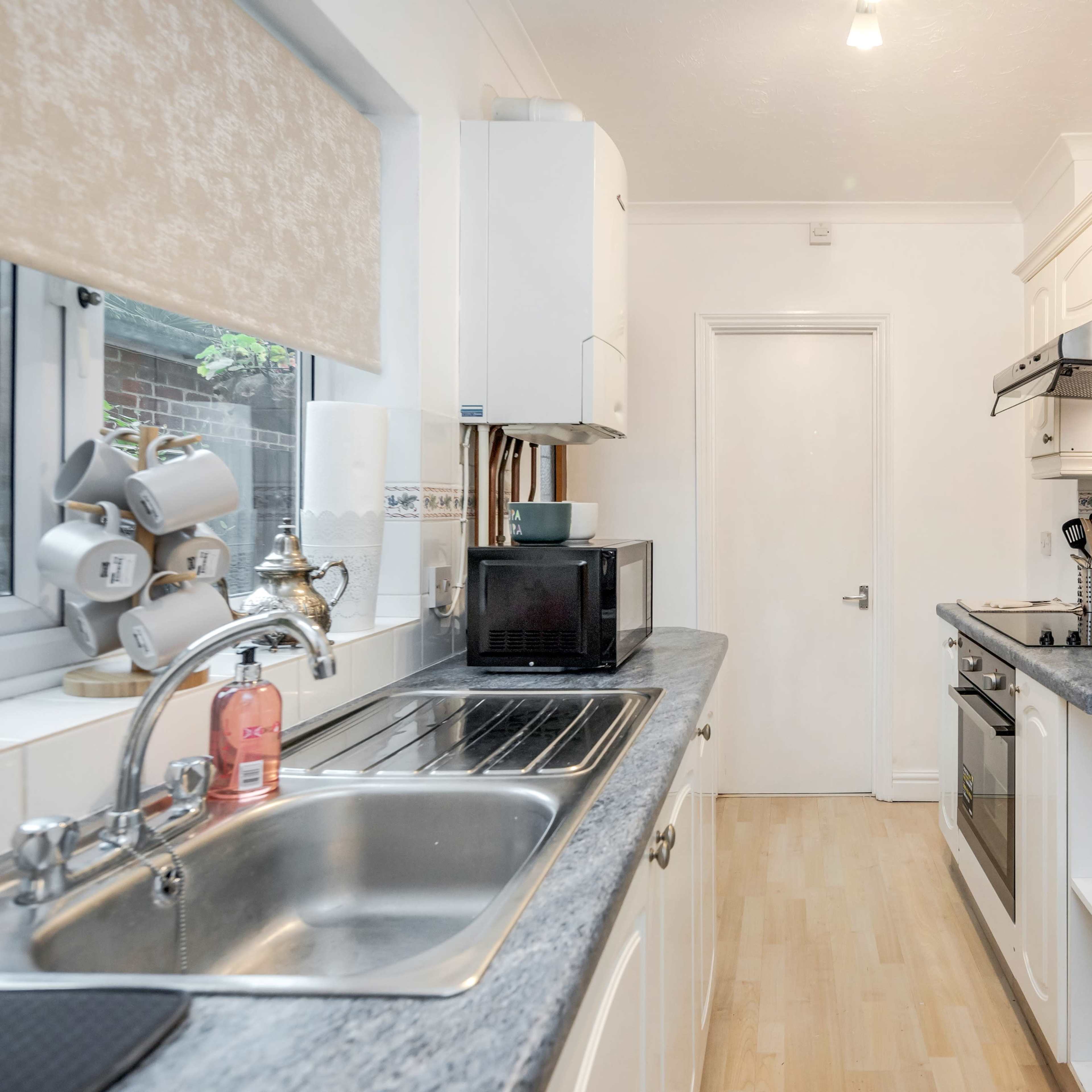 A compact kitchen features white cabinets, a sink, a countertop with a microwave, and a stove along one wall.