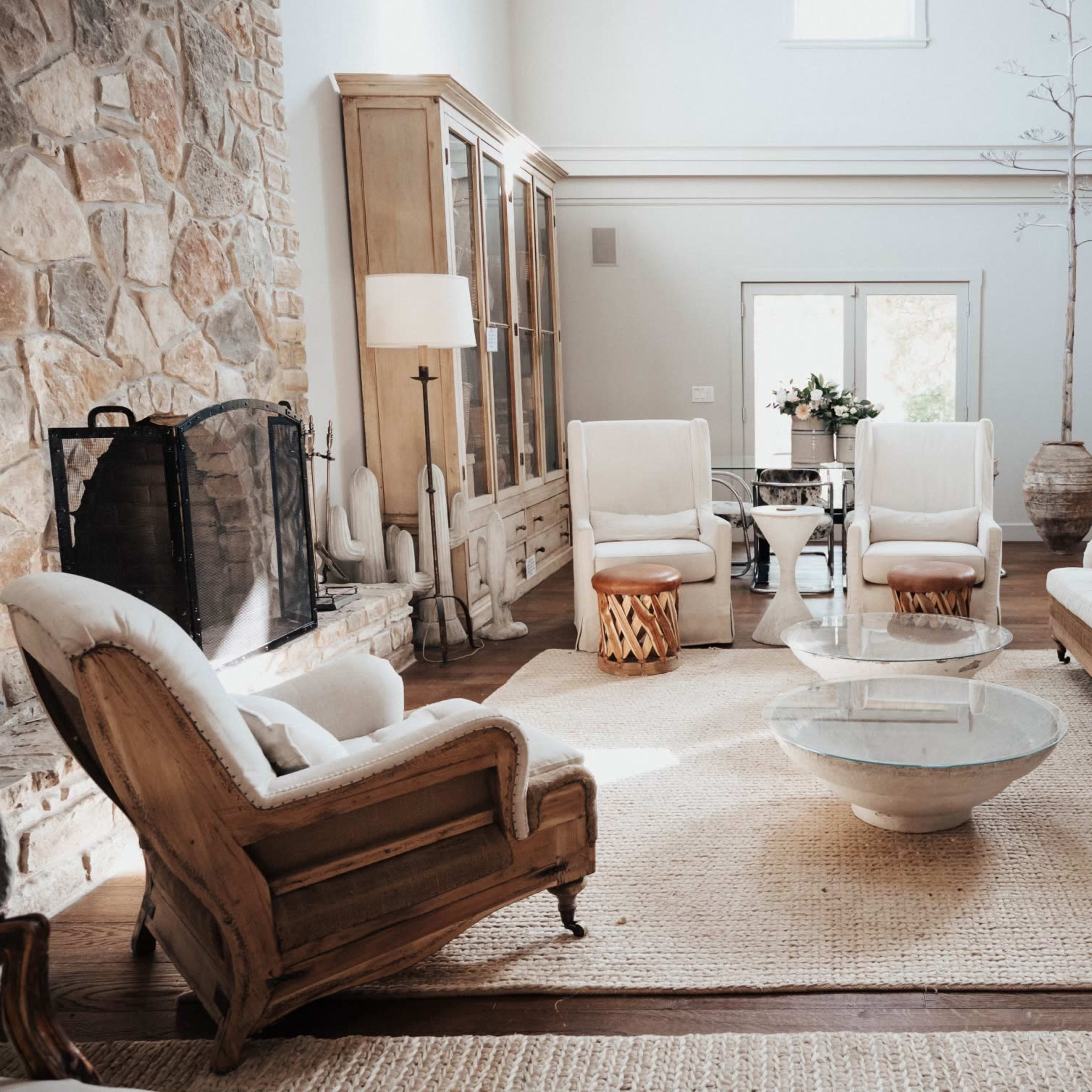The living room features a stone fireplace, a circular glass coffee table, and beige upholstered furniture arranged on a textured rug.