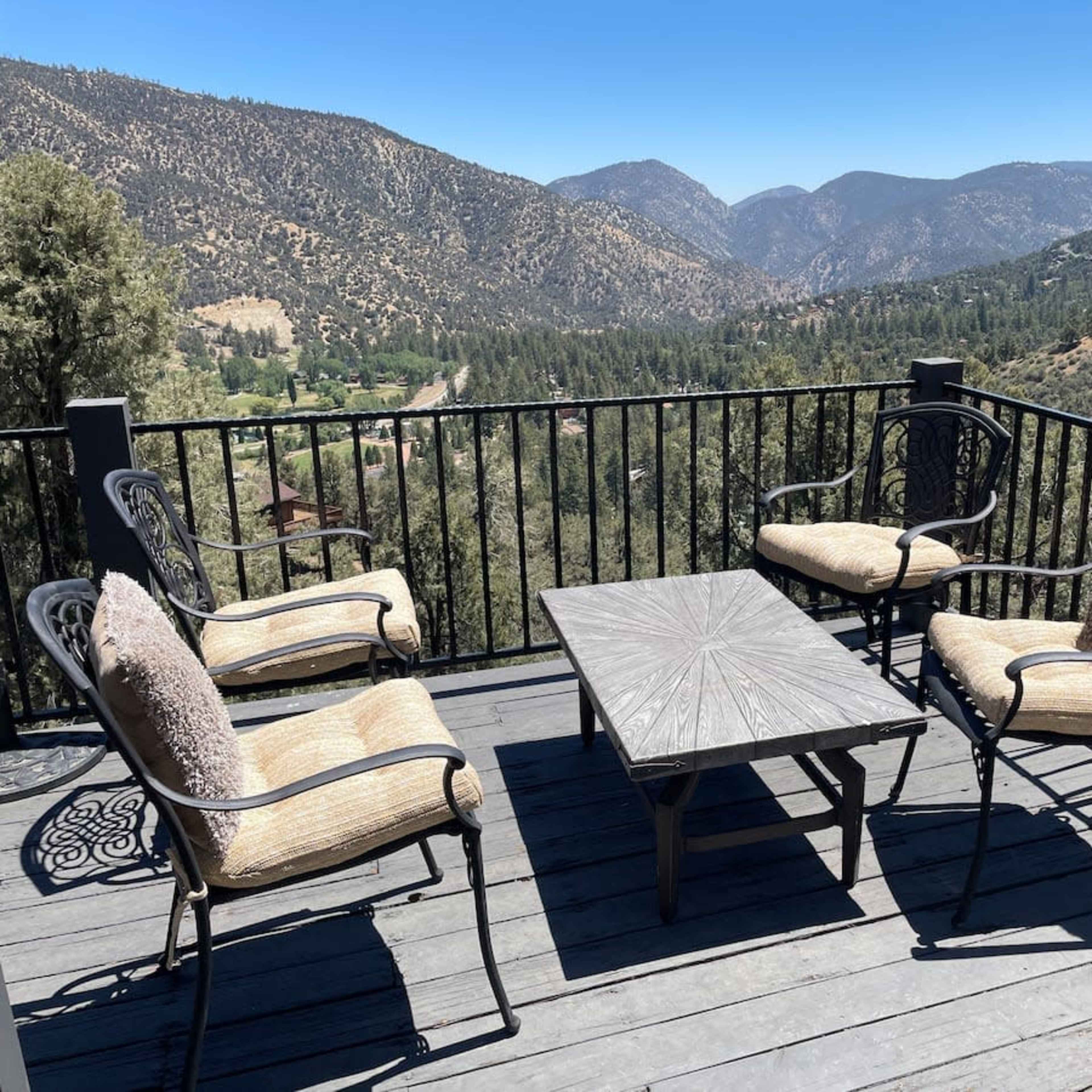 A patio deck with four chairs and a table overlooks a mountainous landscape.