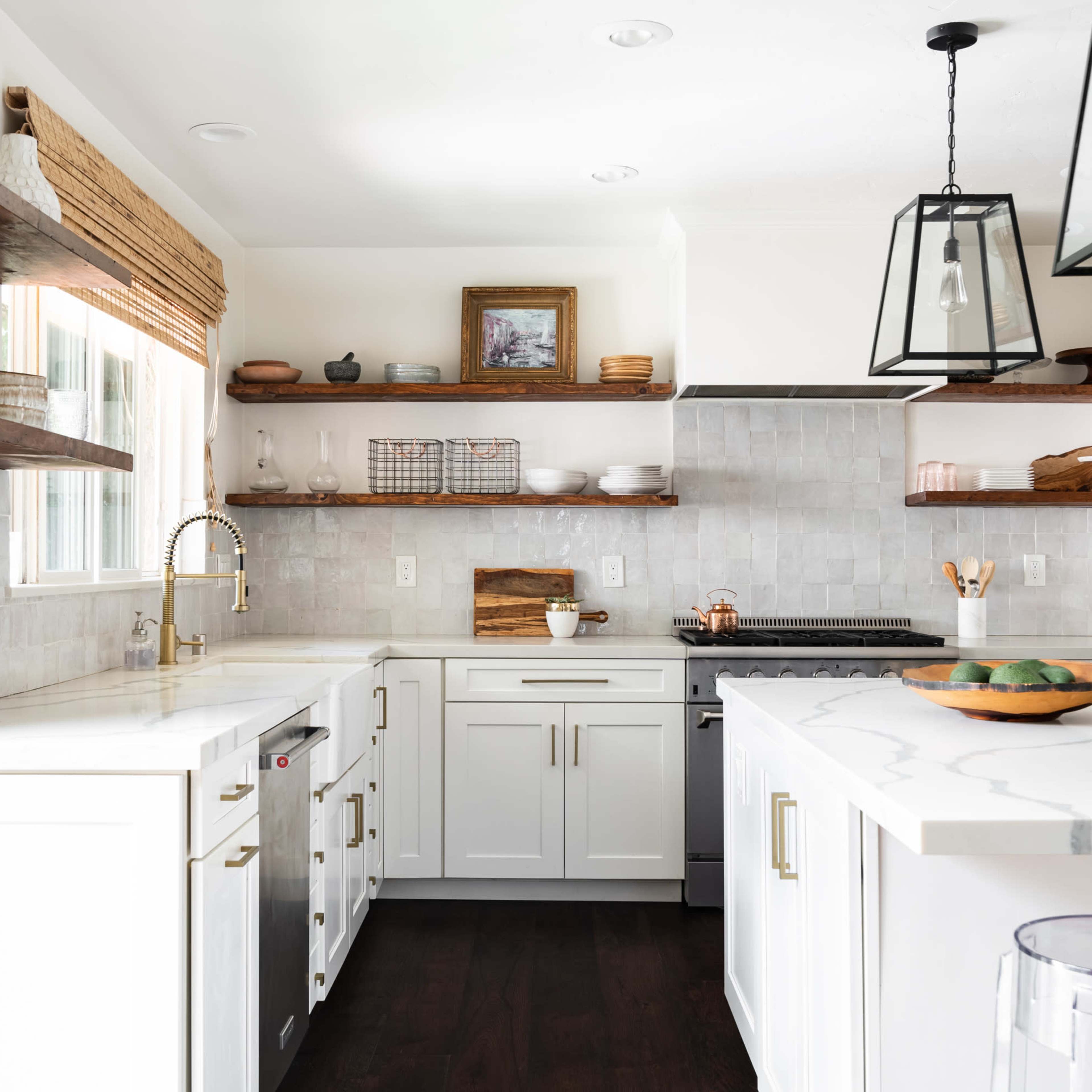 A modern kitchen features white cabinetry, marble countertops, open shelving with decorative items, and stainless steel appliances.