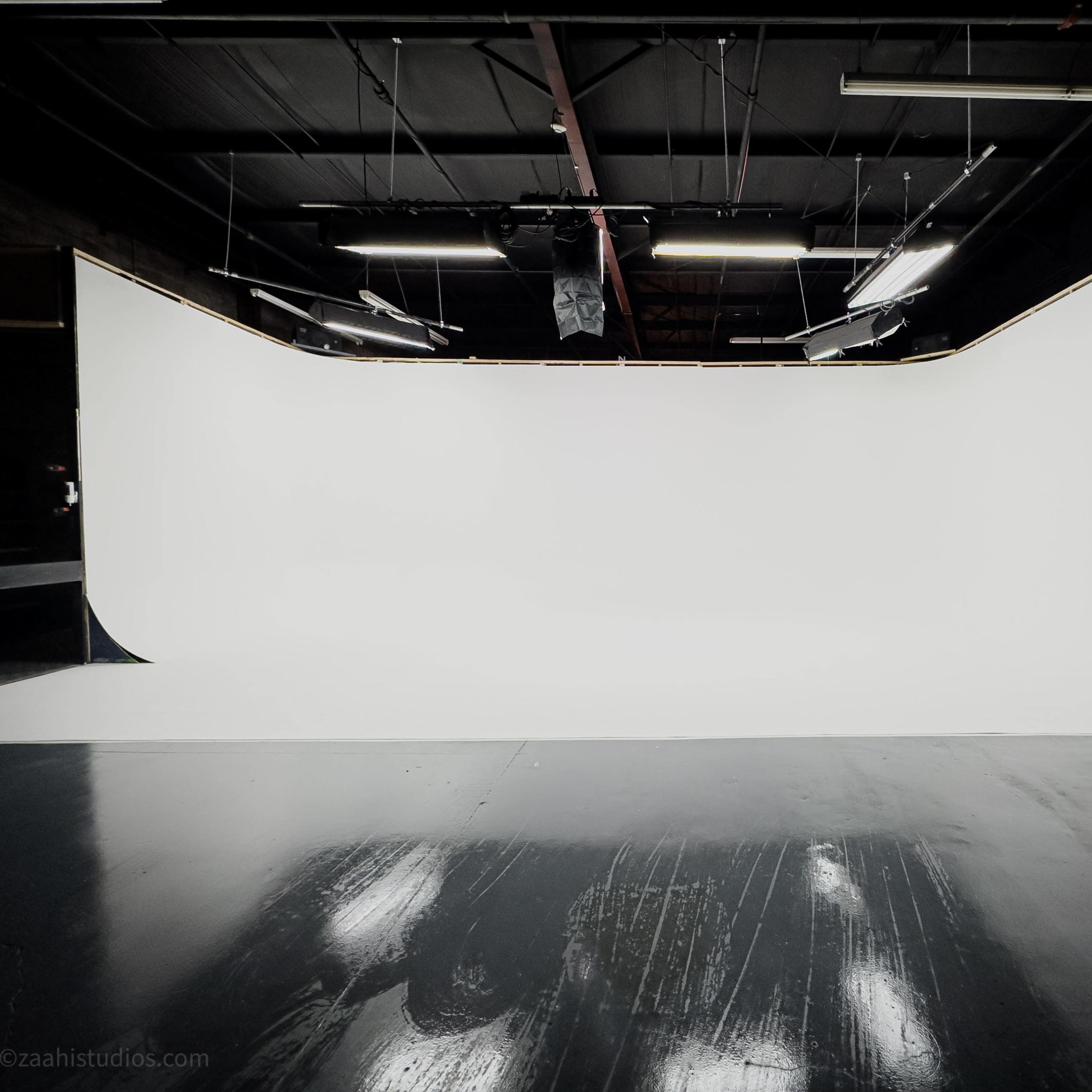 A sleek photography studio features a large, seamless white backdrop and polished black flooring.